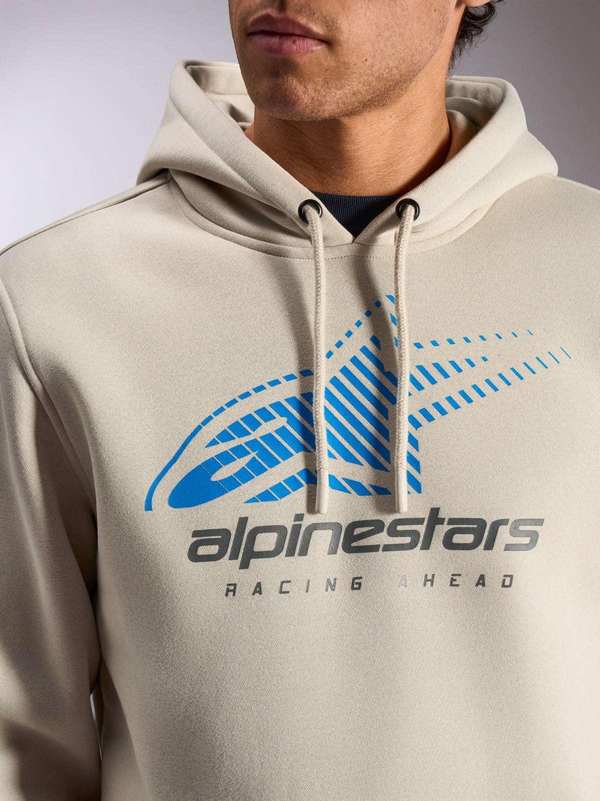Alpinestars Pulse Hoodie, Off White casual streetwear pullover, close-up of chest featuring blue and gray Astars Combo Logo with speed line fade and 'Racing Ahead' text, drawstring hood with dipped tips.