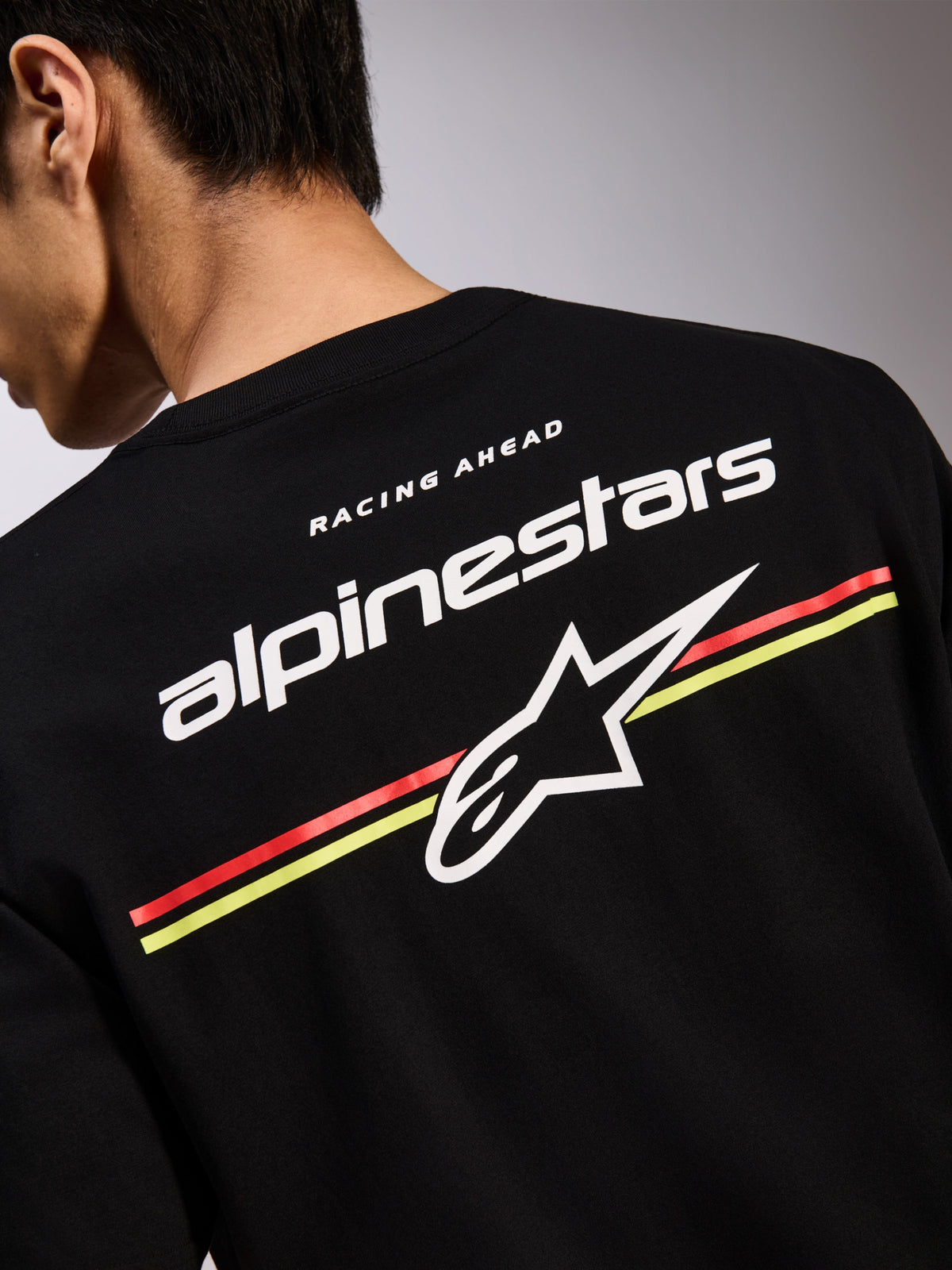 Alpinestars Lanes CSF Tee, Black Short Sleeve T-Shirt, Back Graphic with White Alpinestars and Astars Logos over Red and Yellow Stripes, Casual Motorsport Streetwear