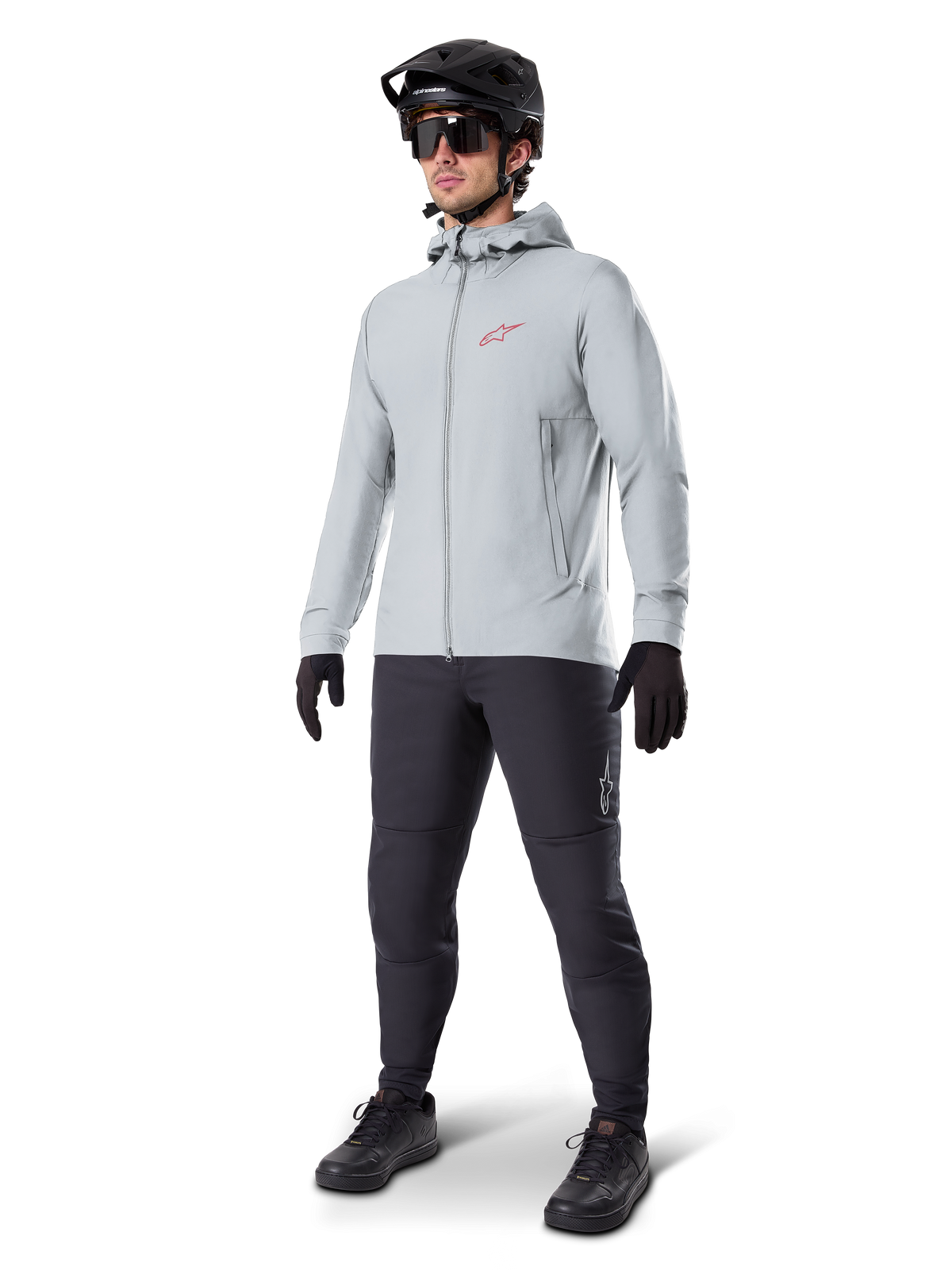 Alpinestars A-Dura Thermal Jacket in Titanium, light gray hooded cycling jacket with a red Alpinestars logo on the chest, worn by a man with a black MTB helmet, sunglasses, dark gray pants, and black gloves, professional mountain bike gear