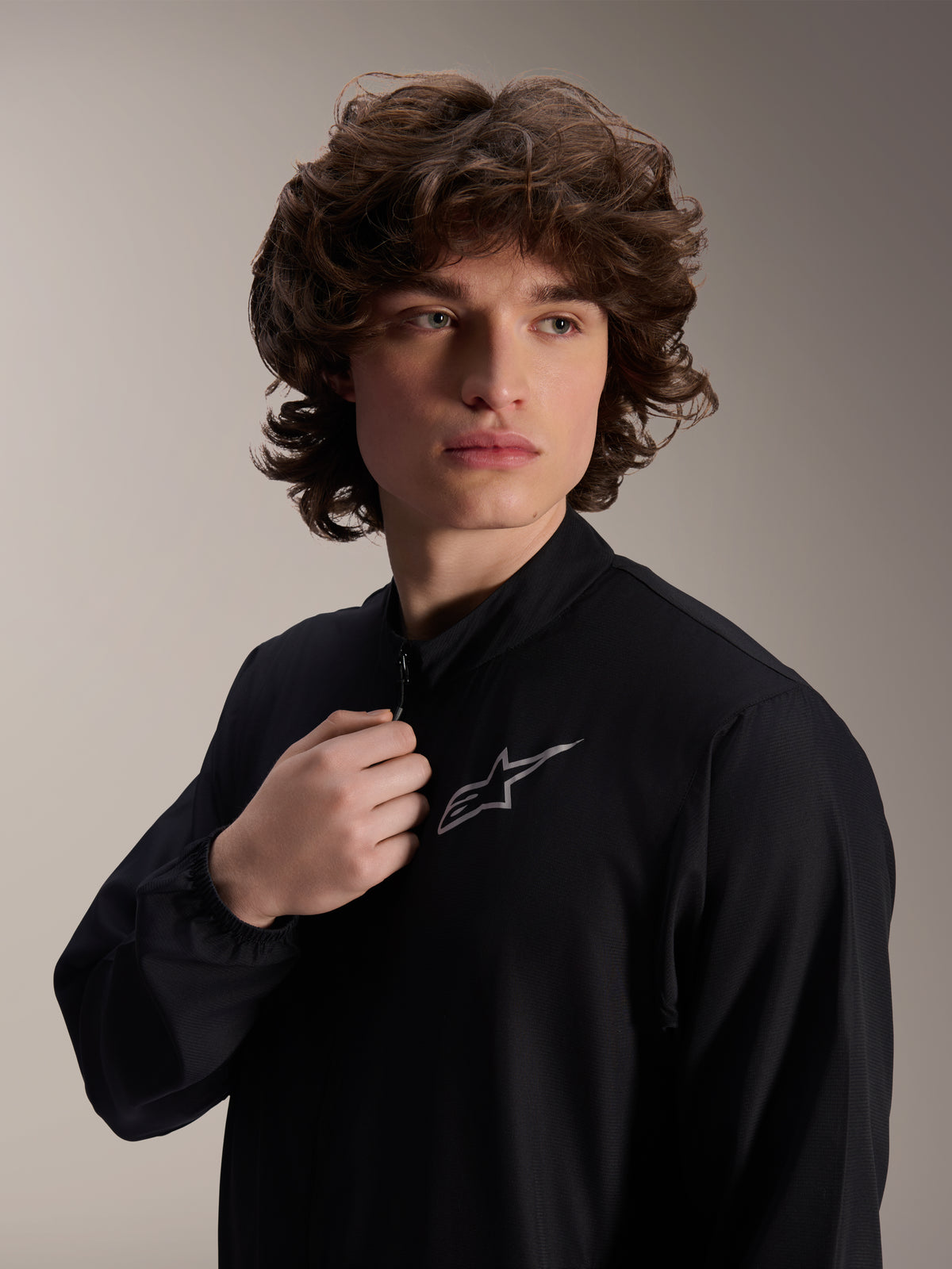 Alpinestars A-Aria Windbreaker Jacket, Black Cycling Jacket, worn by a male model, mock neck design with a silver Astars logo on the chest, lightweight and wind-resistant performance MTB gear