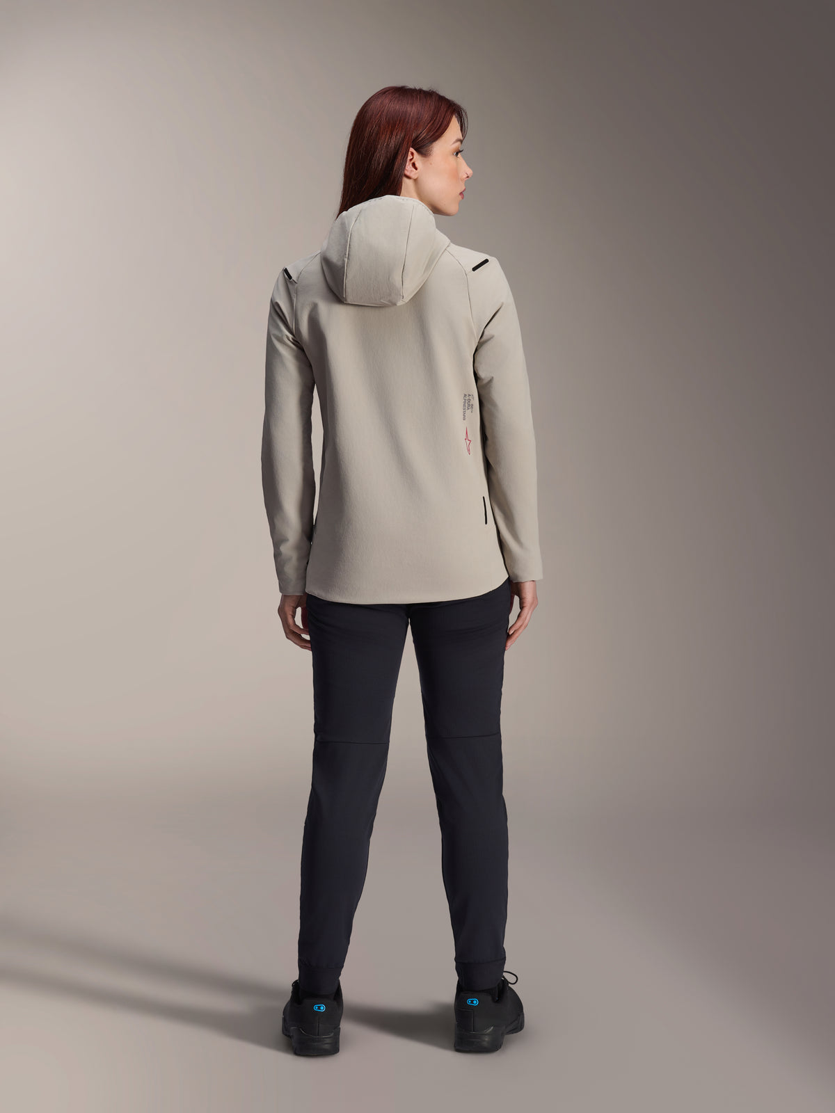 Alpinestars Woman Stella A-Dura Thermal Jacket, Titanium Gray, back view worn with black pants, featuring a fleece-lined insulated hood and a small red logo, functional and stylish mountain bike jacket for cold-weather riding.