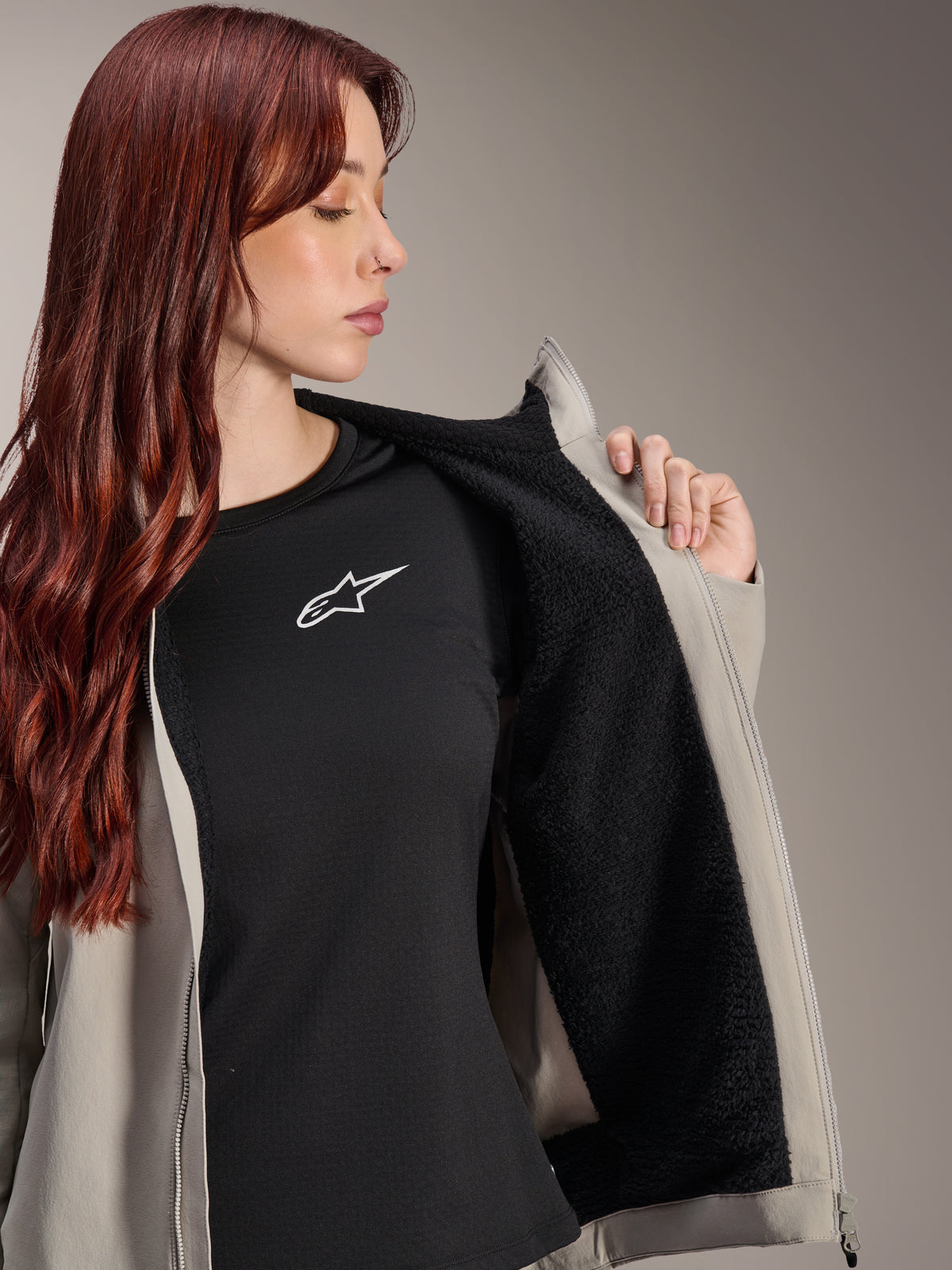 Woman wearing the Alpinestars Stella A-Dura Thermal Jacket in Titanium, showcasing the black textured fleece lining, worn over a black t-shirt with a white star logo, lightweight mountain bike jacket for cold conditions.