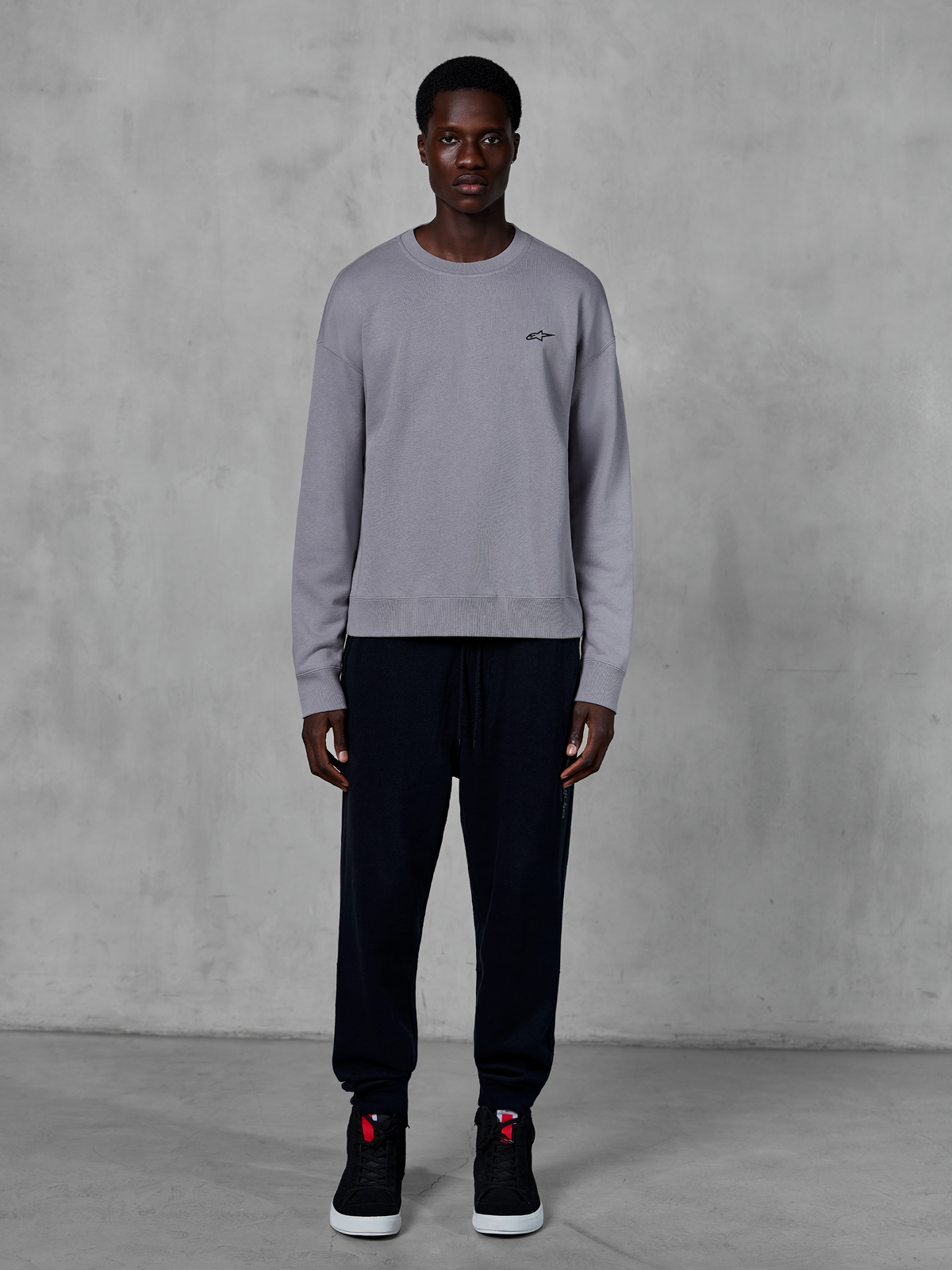 Alpinestars Essentials Ageless Crew, Silver crewneck sweatshirt, worn by a model with black joggers and black sneakers, featuring a small black Alpinestars logo on the chest, casual motorsport-inspired streetwear
