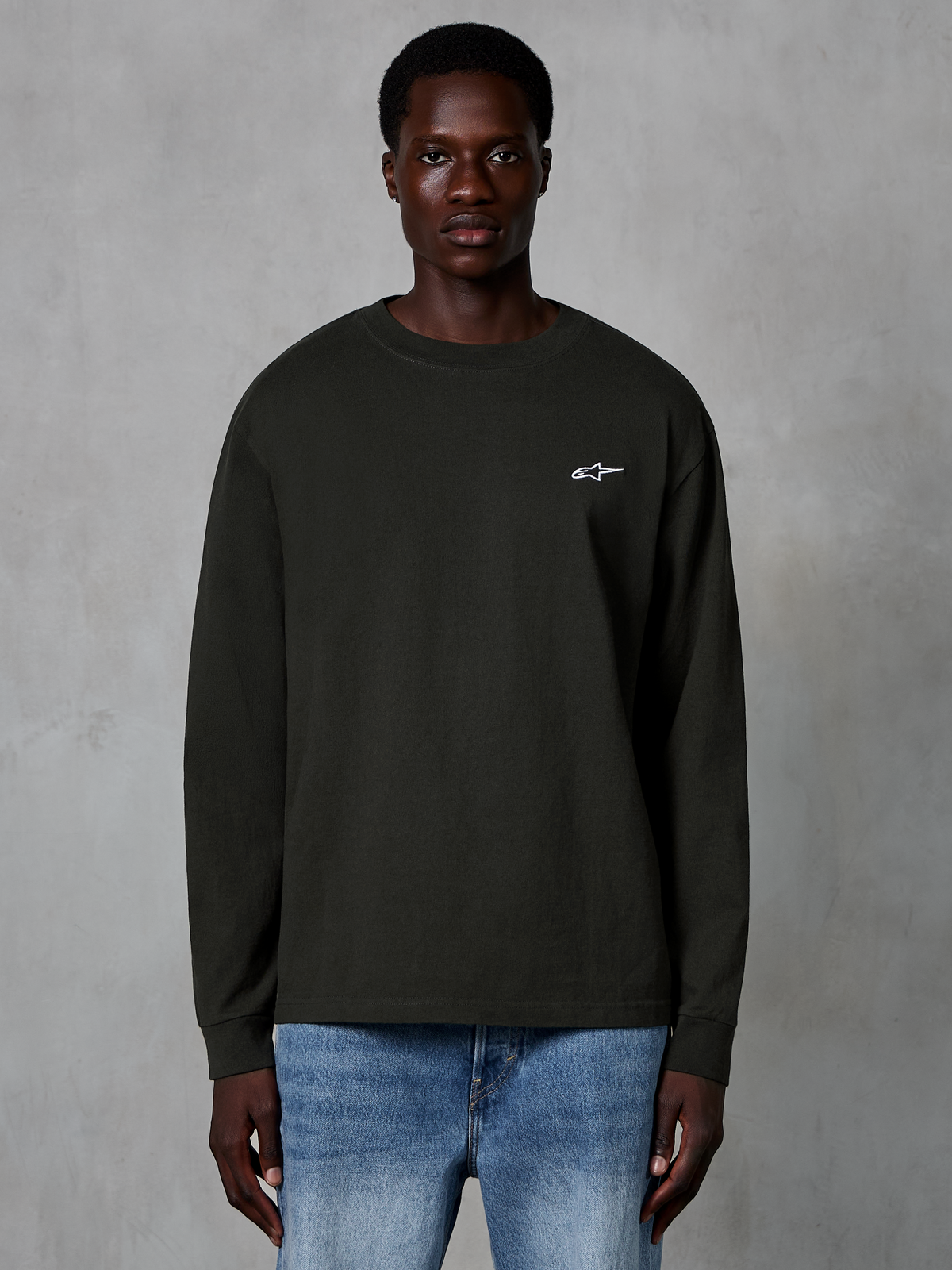 Alpinestars Essentials Ageless LS Tee, Long Sleeve T-Shirt, Off Black, featuring a small white Alpinestars logo on the chest, worn by a model with blue jeans, casual organic cotton streetwear