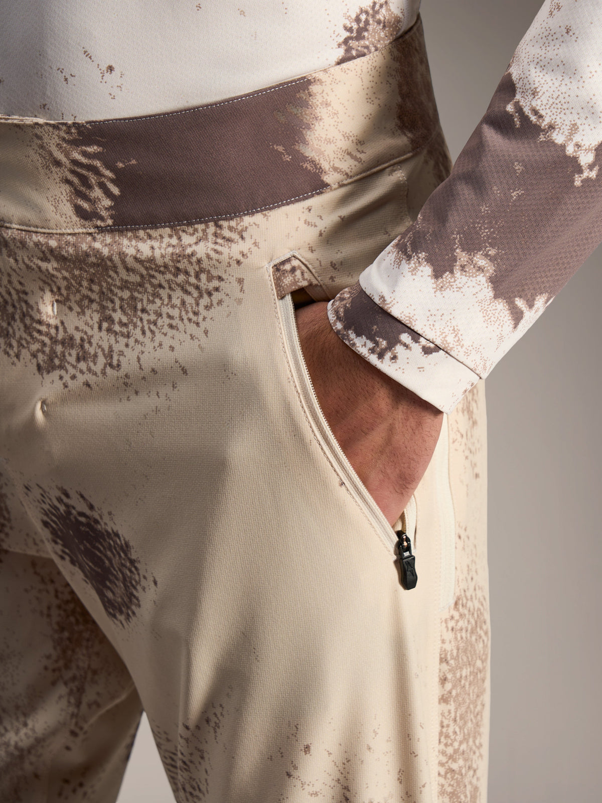 Alpinestars A-Dura Ride Shorts in Sand Camo, showing a zippered side pocket and durable 4-way stretch MTB fabric.