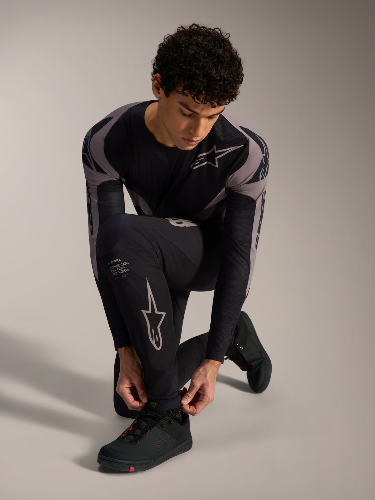 Black Alpinestars A-Supra Elite Pants with grey racing logos, worn by a kneeling model for performance MTB riding.