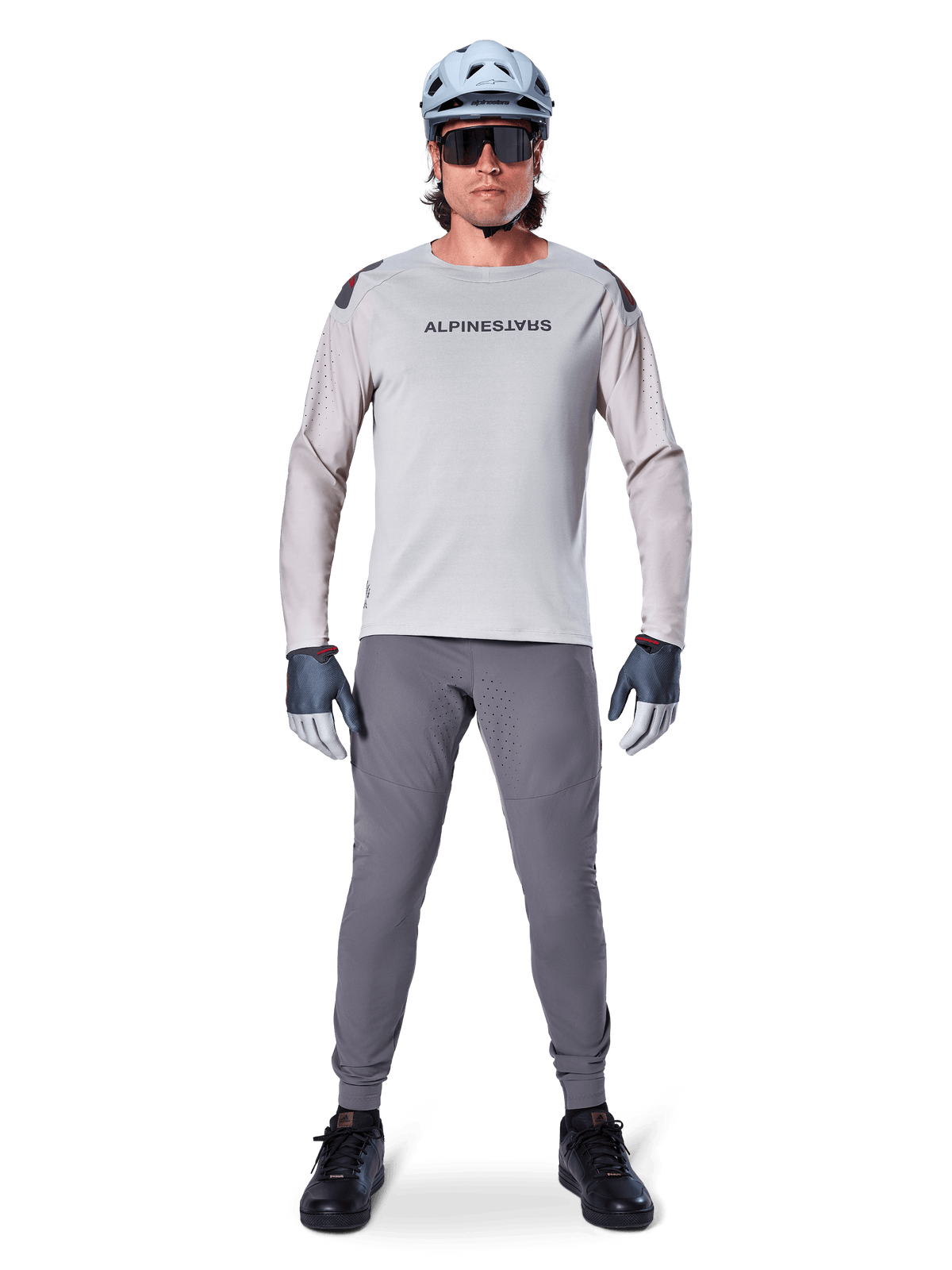 Alpinestars A-Aria Elite Pants, Dark Gray Mountain Bike Pants, worn by a rider in a light gray long-sleeve jersey, light blue helmet, and black shoes, featuring visible laser perforations on the inner legs and a slim performance fit.
