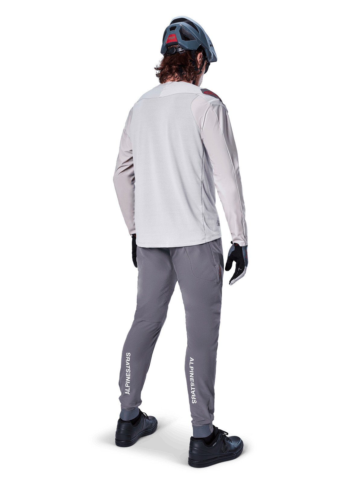 Alpinestars A-Aria Elite Pants, MTB Cycling Pants, Dark Gray, rear view of a rider wearing a full outfit, featuring white Alpinestars branding on the lower legs, performance fit with laser perforations, paired with a light gray long-sleeve jersey and gray MTB helmet
