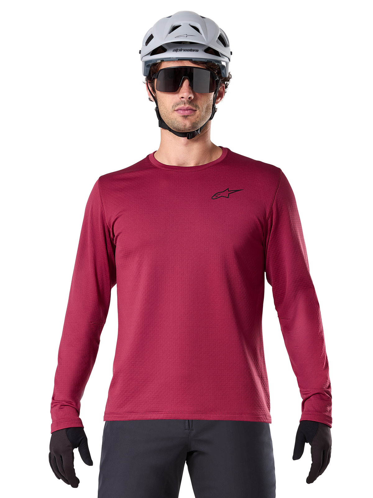 Male cyclist wearing Alpinestars A-Dura Thermal Jersey, Long Sleeve MTB Jersey, Burgundy, styled with a gray helmet and black sunglasses, features a small black star logo on the chest, insulated fleece fabric for cold-weather mountain biking