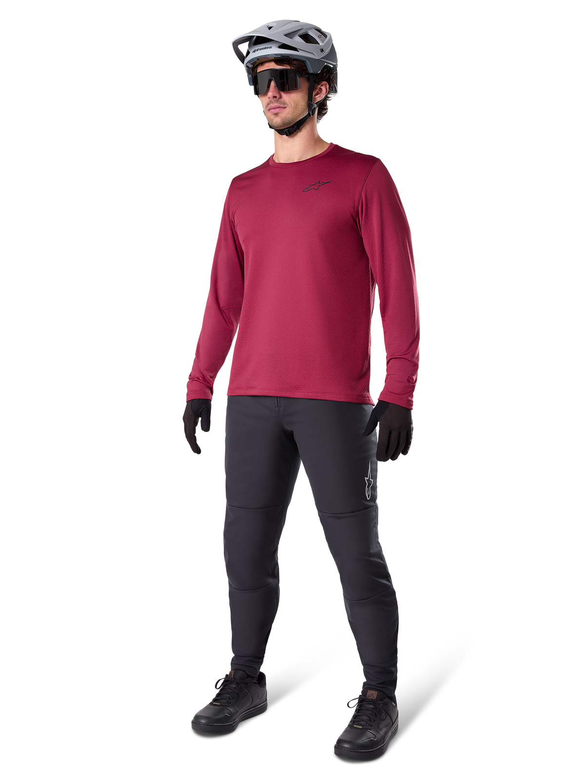 Alpinestars A-Dura Thermal Jersey in Burgundy, long-sleeve insulated cycling top worn with dark grey mountain bike pants, black gloves, and a grey helmet, full-body studio shot of cold-weather MTB gear.