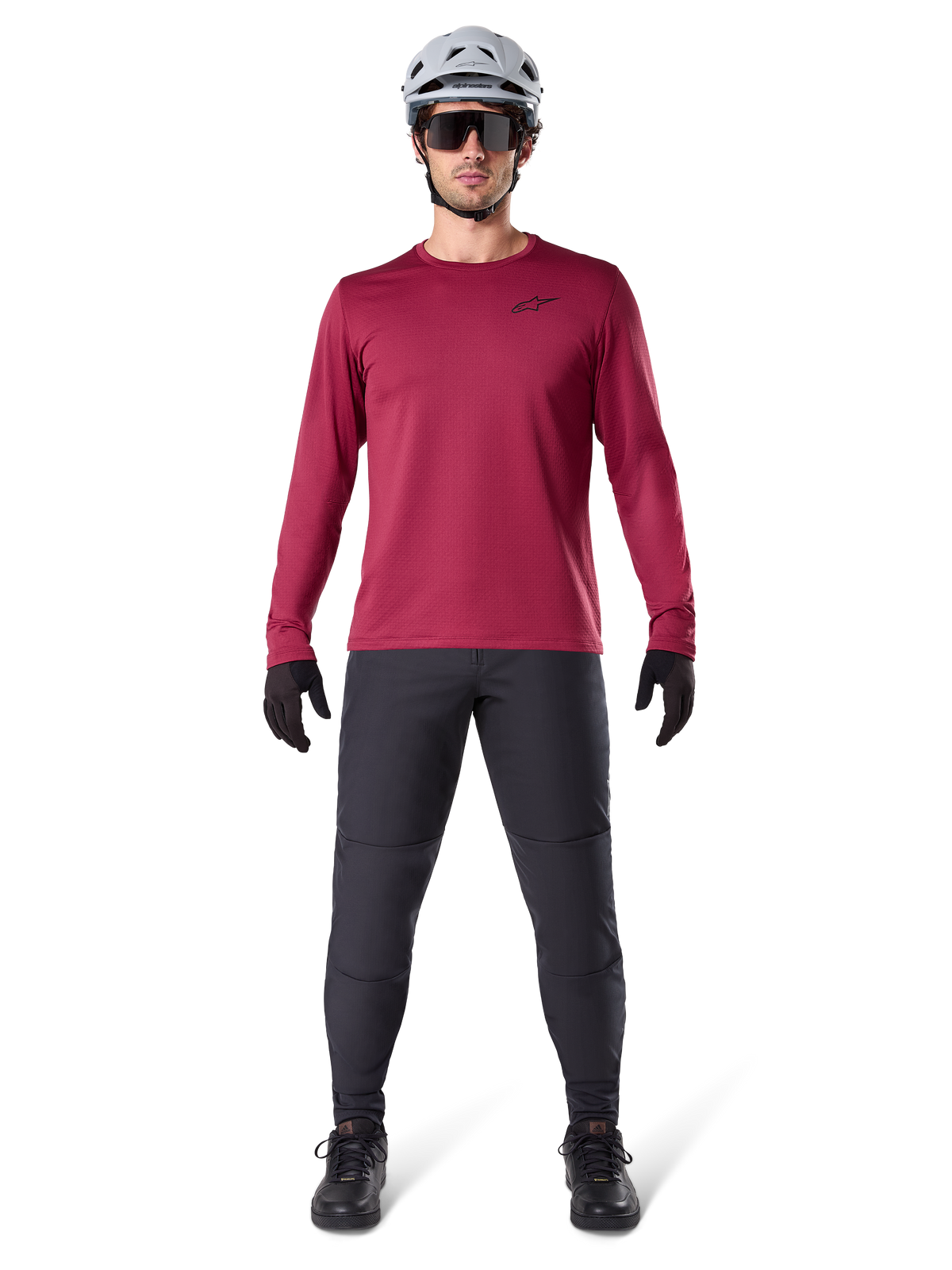Male model wearing Alpinestars A-Dura Thermal Jersey in Burgundy, long-sleeve insulated cycling top, paired with dark grey mountain bike pants, white helmet, black sunglasses, and black gloves, professional MTB gear for cold weather