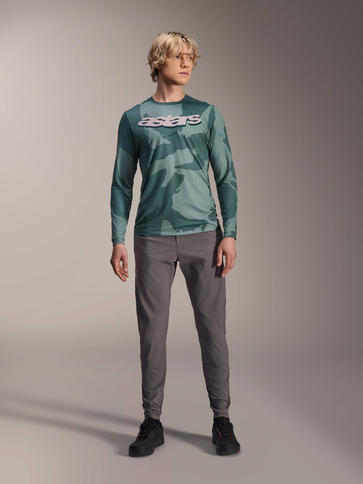 Alpinestars A-Dura Hollow Camo Long Sleeve Jersey, Silver Pine Camo with green camouflage pattern, large white "astars" logo on the chest, worn with gray technical pants and black riding shoes, high-performance MTB gear