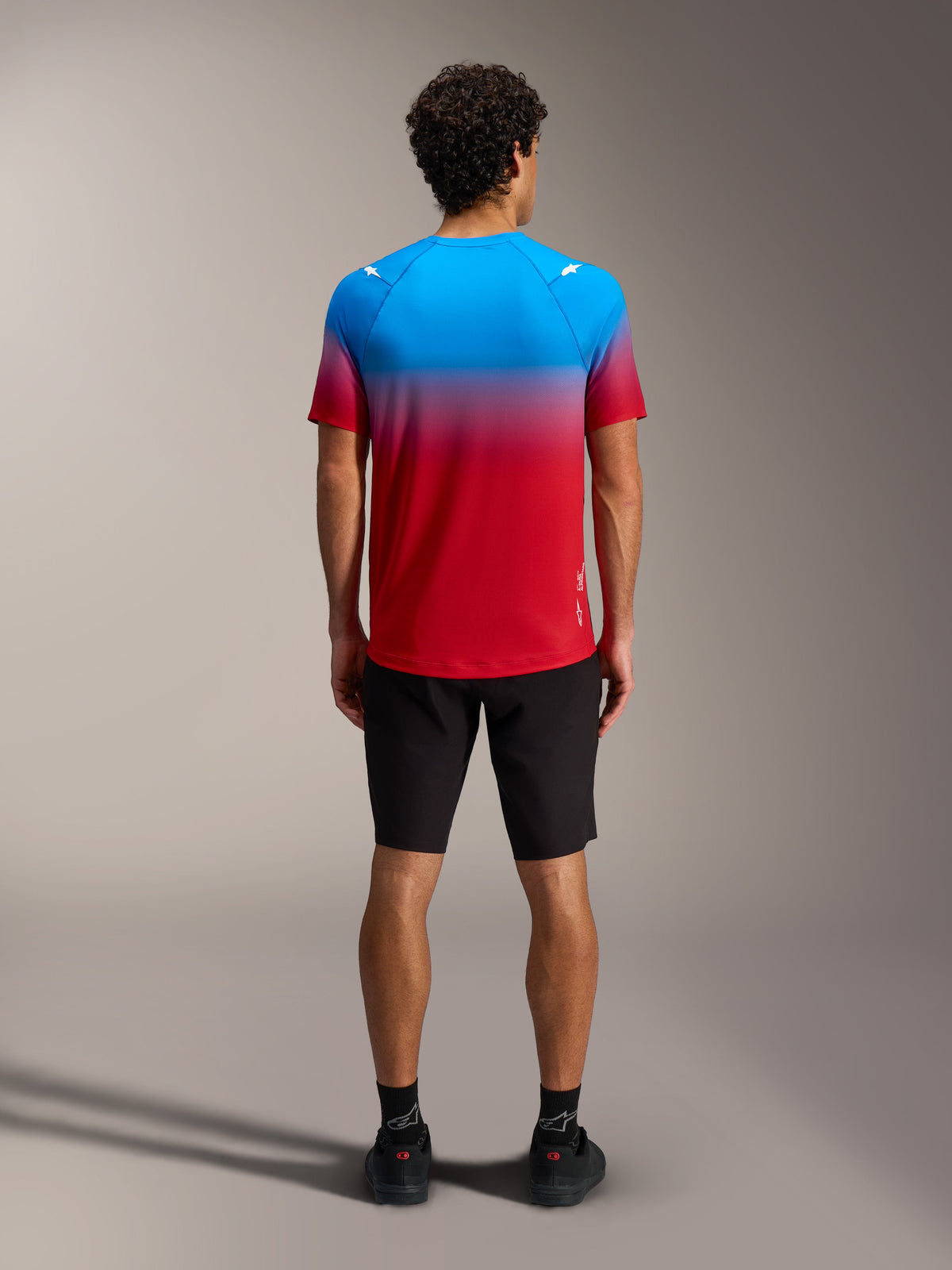 A-Dura ASTARS Jersey 2.0 in red and blue gradient, short sleeve MTB top shown from the back with black shorts.