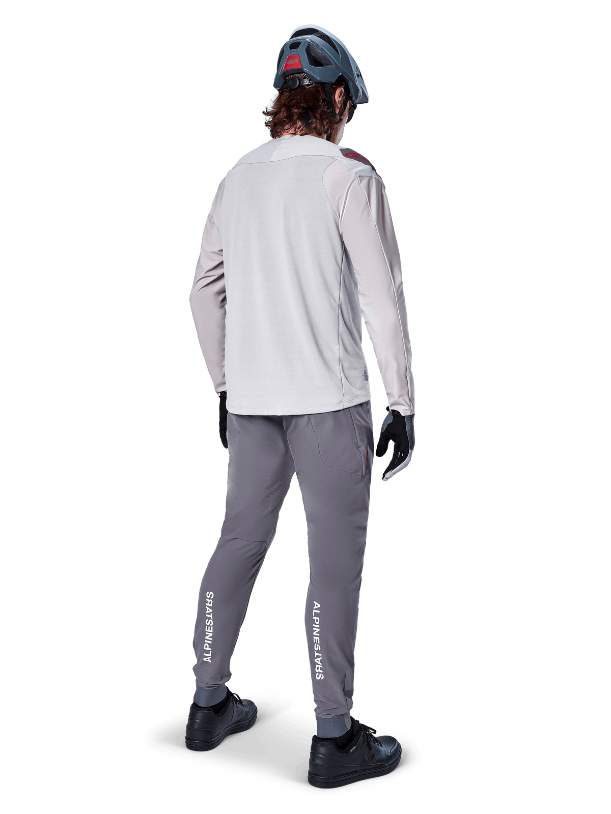 Rear view of a cyclist wearing the Alpinestars A-Aria Polartec Switch Long Sleeve Jersey in Light Gray, paired with dark gray mountain bike pants featuring white Alpinestars branding on the calves, black gloves, and a gray helmet.