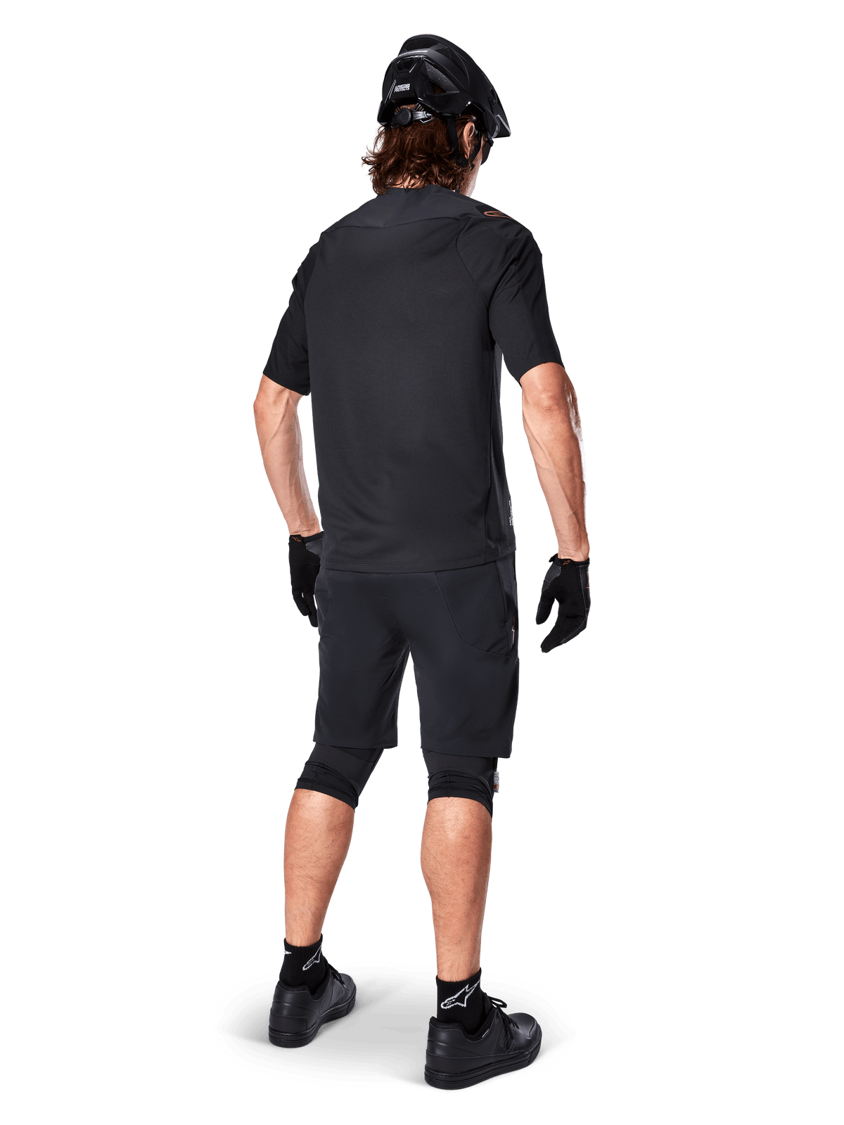 Male mountain bike rider from the back wearing the Alpinestars A-Aria Polartec Switch Jersey in black, short sleeve MTB jersey, paired with black mountain bike shorts, black helmet, and gloves, coordinated performance outfit for off-road trail riding
