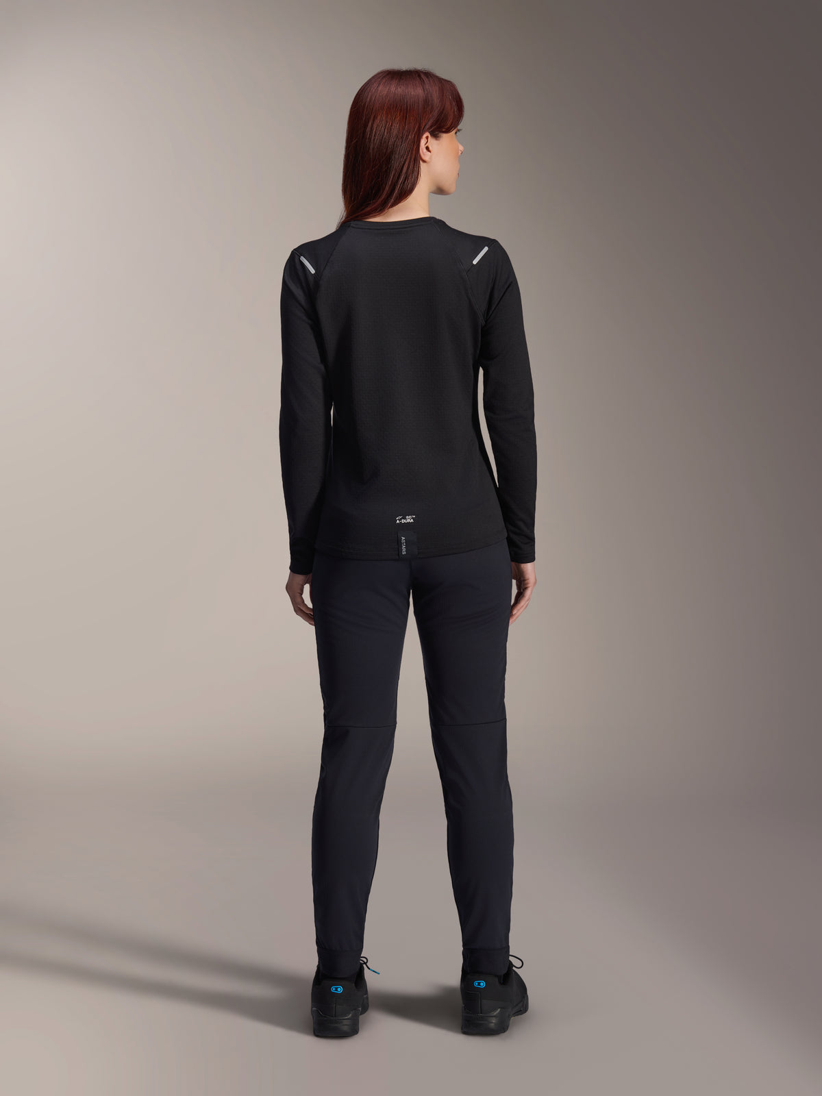 Alpinestars Woman Stella A-Dura Thermal Jersey, Back View, Black, Long-sleeve cycling jersey with insulated fleece, worn with matching black pants and shoes, featuring small A-Dura branding on the lower back and reflective shoulder accents, tailored for women's MTB riding.