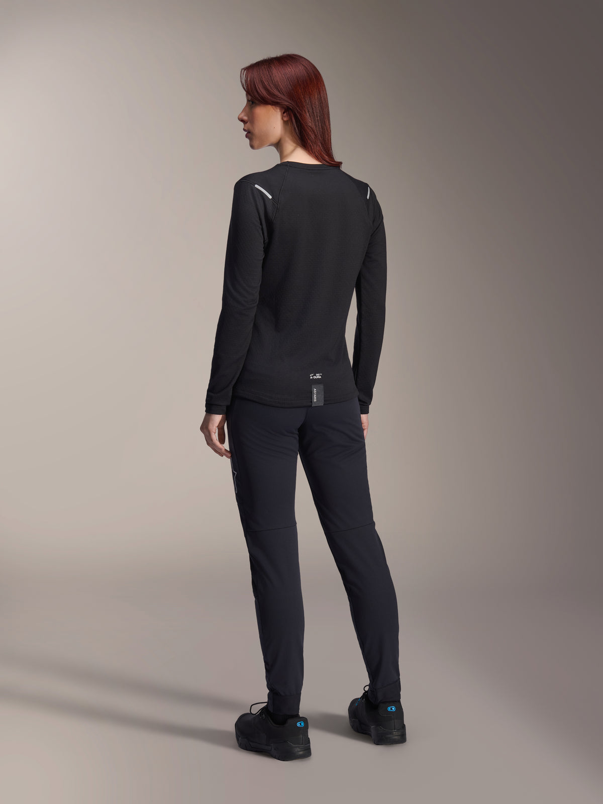 Alpinestars Woman Stella A-Dura Thermal Jersey, long-sleeve MTB jersey in Black, rear view showing reflective shoulder accents and extended drop tail, worn with black pants and shoes, performance gear for mountain biking.