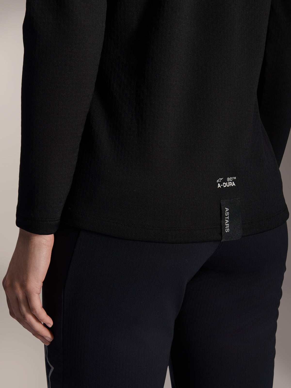Alpinestars Woman Stella A-Dura Thermal Jersey, Black Thermal MTB Jersey, close-up of back lower hem with white A-DURA branding and vertical ASTARS logo tag, designed for cold weather mountain biking