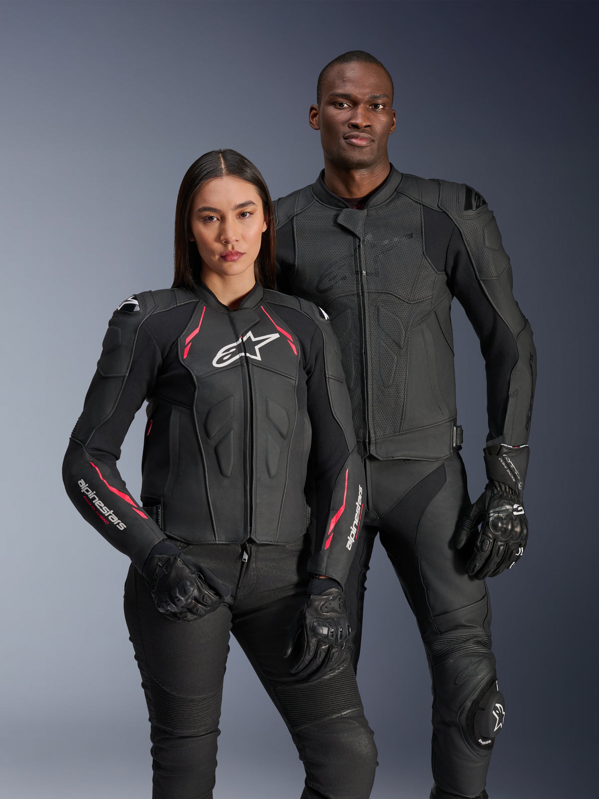 Alpinestars Stella Dusk Leather Jacket, Black Diva Pink White, worn by a female model alongside a male model in matching black leather gear, featuring pink and white accents, white star logo on chest, and black riding gloves
