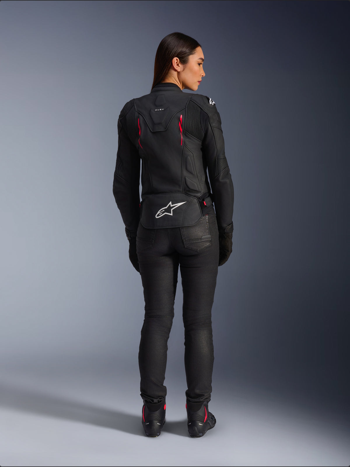 Alpinestars Stella Dusk Leather Jacket, rear view, black leather with Diva Pink and White accents, features white Alpinestars logo on lower back and pink vent details, worn with black riding pants and boots, premium sport motorcycle gear for women