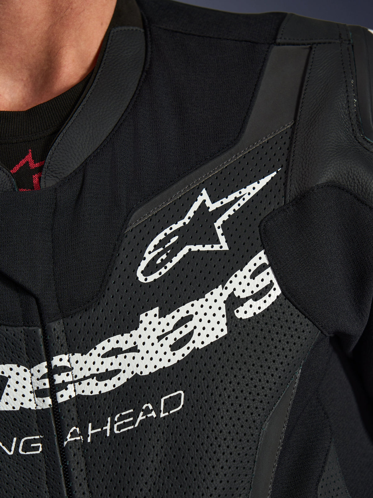 Alpinestars GP Force V2 Leather Suit 1-Piece, close-up of chest area, Black perforated leather with large white Alpinestars logo, technical sport riding gear, detailed texture and branding
