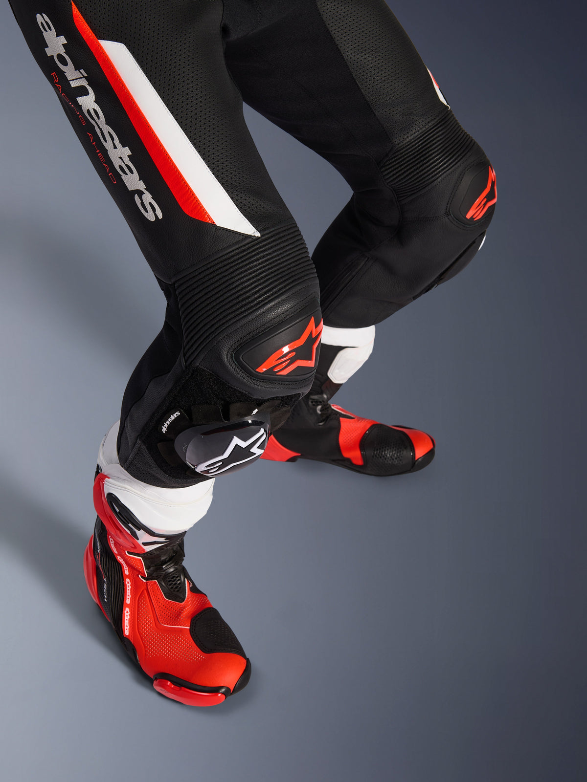 Alpinestars GP Force V2 1-Piece Leather Suit, Black White and Red Fluo, close-up of lower legs and knees featuring DFS Lite protectors and replaceable sliders, paired with professional racing boots