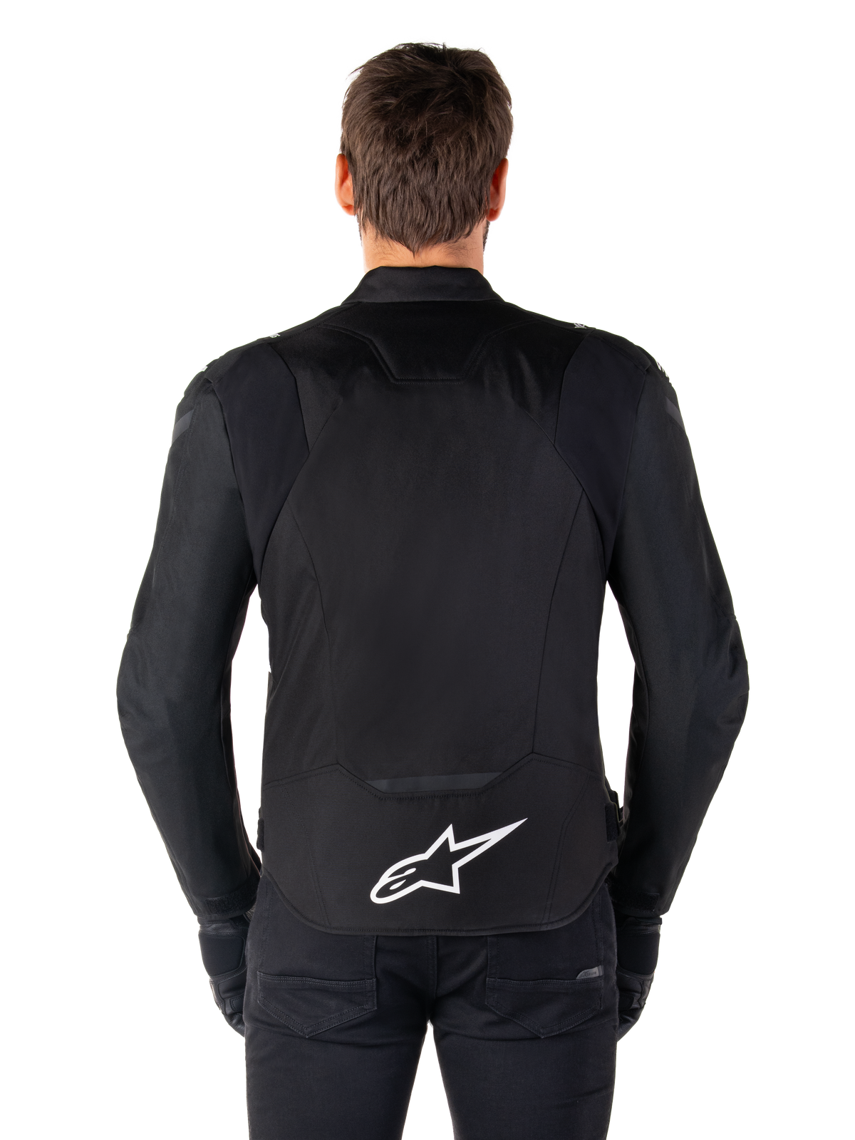 Alpinestars T-Jaws V4 Waterproof Jacket, Black motorcycle jacket seen from the back, featuring a white Alpinestars logo on the lower back, extended rear for coverage, worn by model with black pants and gloves, sleek sport textile design