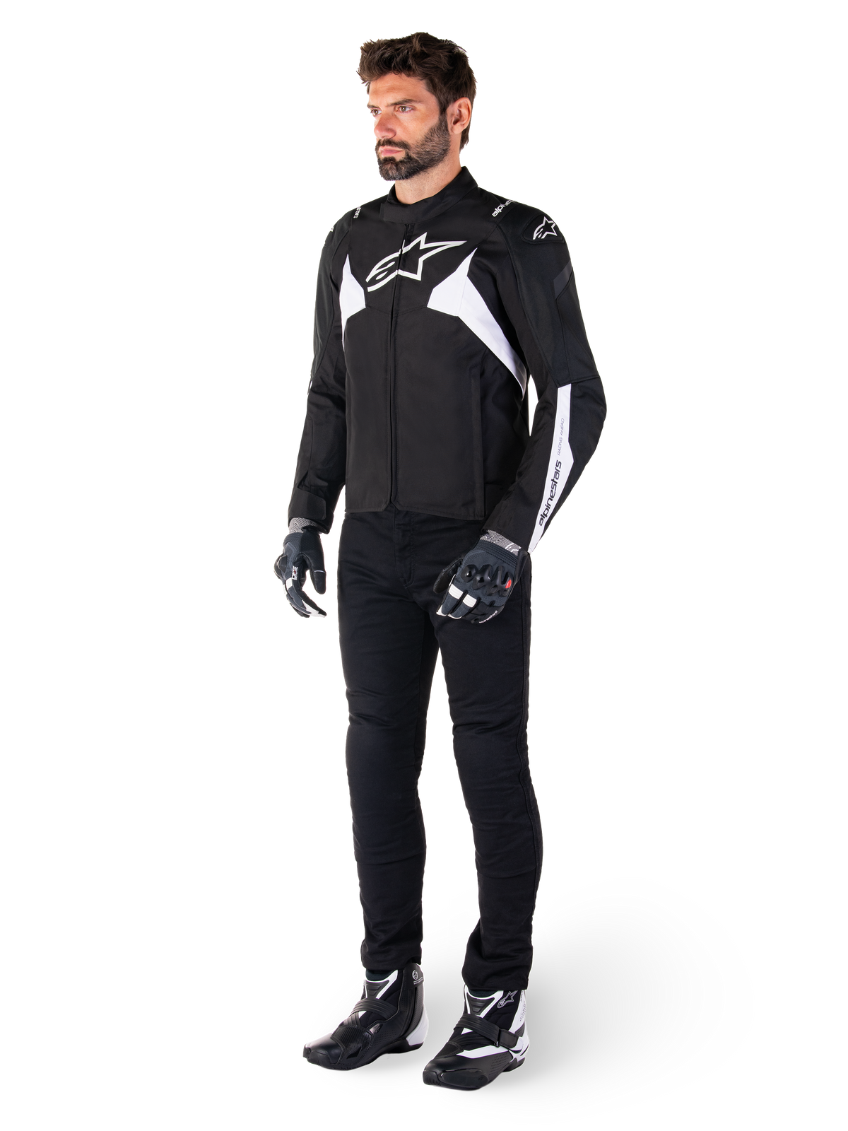 Male model wearing Alpinestars T-Jaws V4 Waterproof Jacket in Black and White, sport textile jacket featuring a white star logo and sleeve accents, styled with black motorcycle pants, gloves, and boots for a complete road riding look.