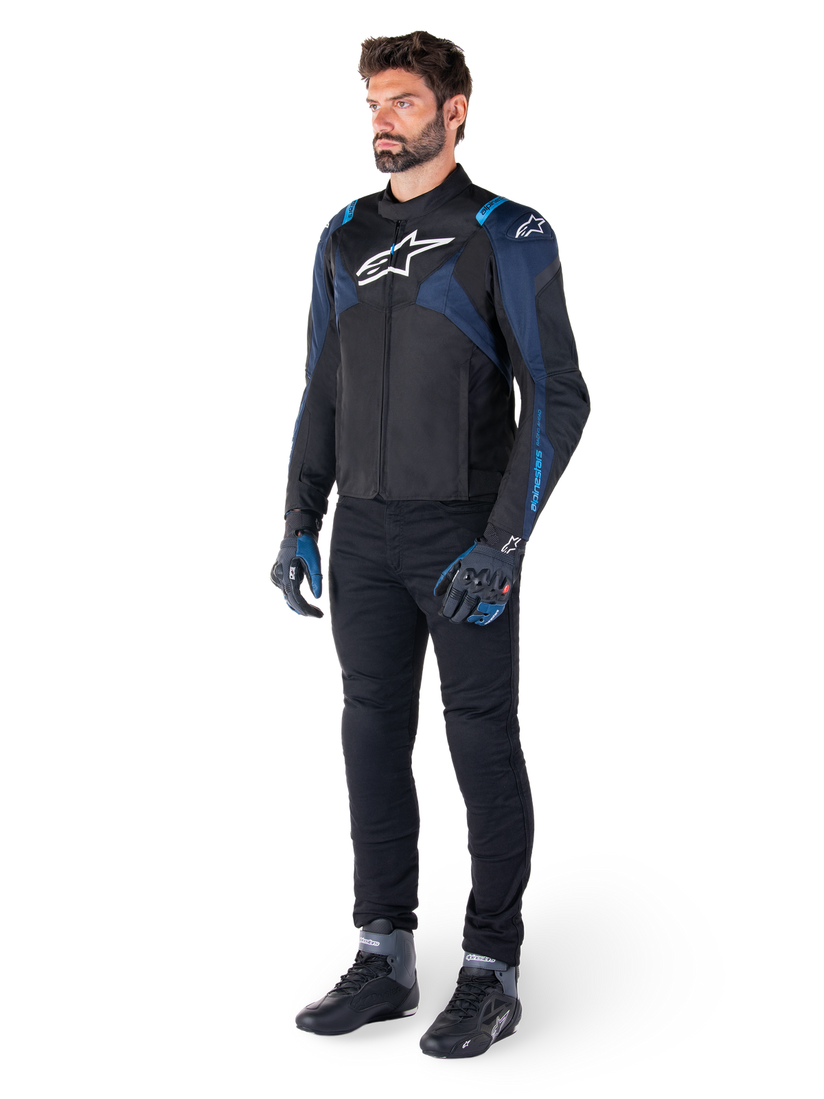 Alpinestars T-Jaws V4 Waterproof Jacket in Black, Dark Blue, and Blithe Blue, worn by a model with black motorcycle pants and riding boots, featuring white Alpinestars logo on chest and blue shoulder accents, sport-fit riding gear.