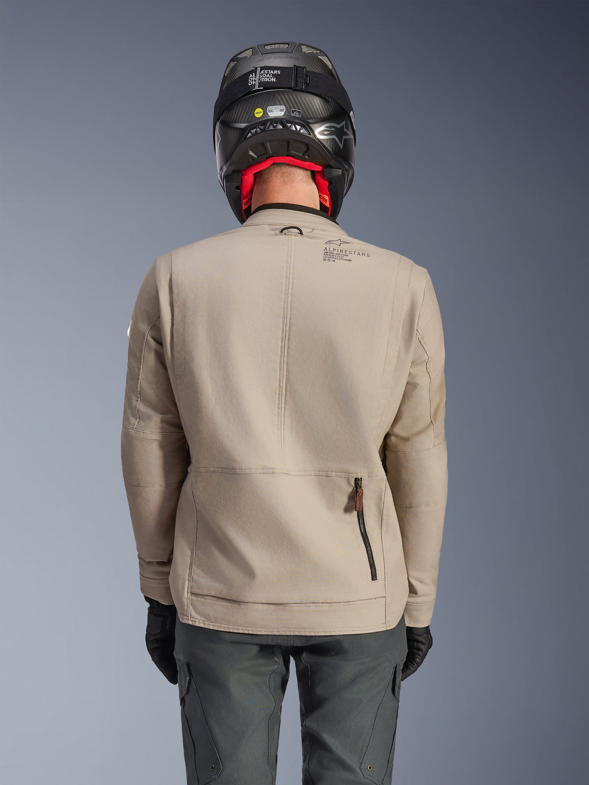 Alpinestars Borrego Drystar® Jacket, Adventure Motorcycle Jacket, Warm Gray, back view showing rear compartment zipper and Alpinestars branding, worn with a black helmet and charcoal riding pants