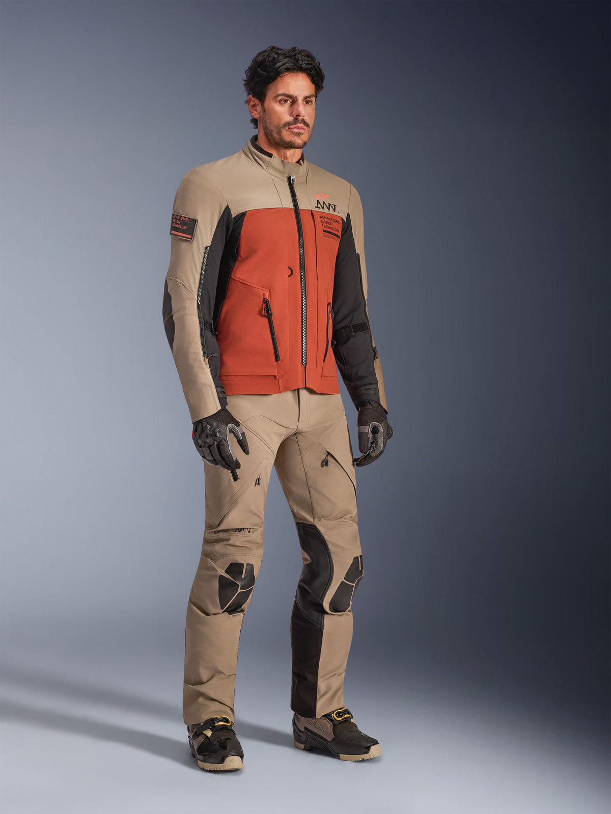 Alpinestars AMT-8 Stretch Drystar® XF Jacket, Walnut Rust Black adventure riding jacket, worn with matching technical pants and gloves, featuring a multi-tonal design with tan, rust orange, and black panels, designed for long-range motorcycle touring.
