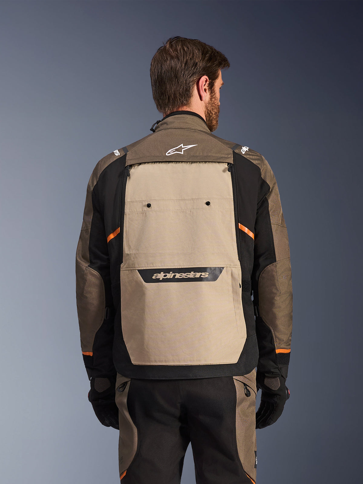 Alpinestars Cusco Drystar® Jacket, Walnut Aluminum Black, rear view, featuring a large tan back panel with black logo, orange accents, worn with matching pants and gloves, designed for adventure touring.