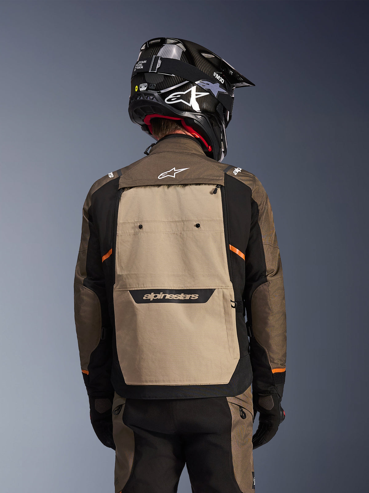 Rear view of the Alpinestars Cusco Drystar® Jacket in Walnut Aluminum Black, adventure touring motorcycle jacket featuring a large tan back panel with Alpinestars branding, black sleeves with orange accents, shown with a black carbon-style helmet.