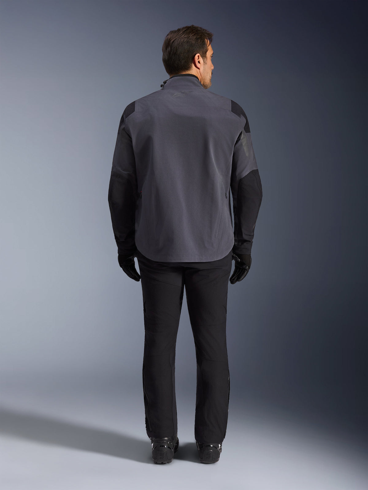 Alpinestars Maxdura Drystar®XF Laminated Armored Shell, Motorcycle Jacket, Deep Gray and Black, back view of a rider wearing full adventure gear, technical laminated shell with black reinforced shoulder and elbow panels, paired with black pants and gloves.