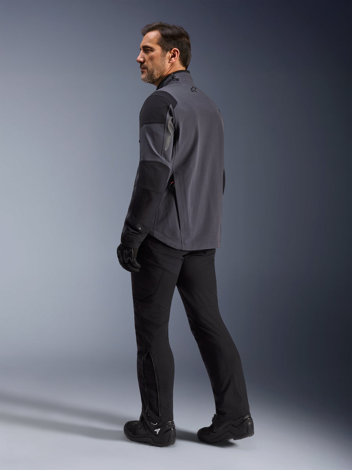 Alpinestars Maxdura Drystar®XF Laminated Armored Shell, Adventure Motorcycle Jacket, Deep Gray and Black, rear view on model looking over shoulder, worn with black riding pants and boots, technical 3-layer laminated design for all-weather performance