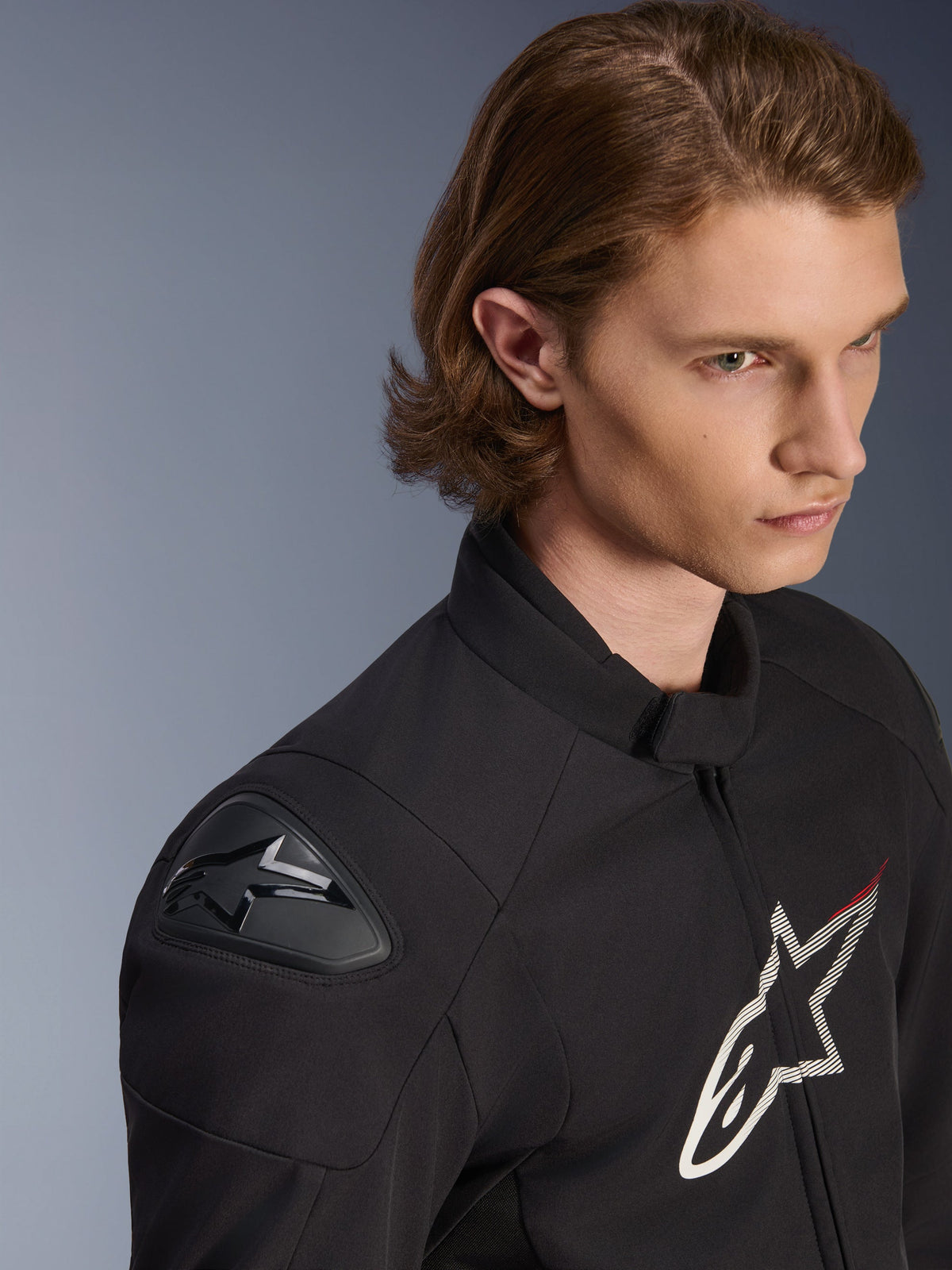 Alpinestars SMX Waterproof Jacket, Black with white and red accents, close-up lifestyle shot on a male model, featuring external DFS Lite shoulder sliders and large star logo on the chest, sport motorcycle riding apparel