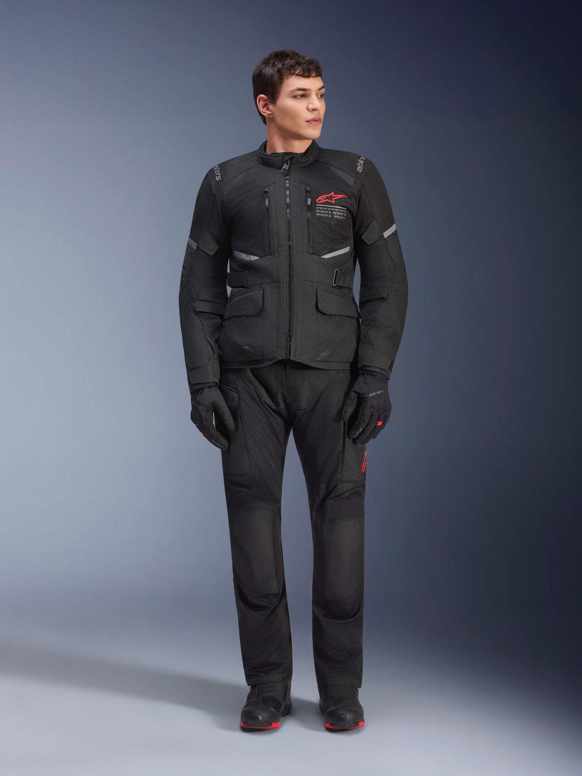 Male model wearing Alpinestars Andes Air Drystar® Jacket in Black, adventure touring motorcycle gear with matching pants and gloves, featuring red logo on the chest, mesh ventilation, and functional pockets.