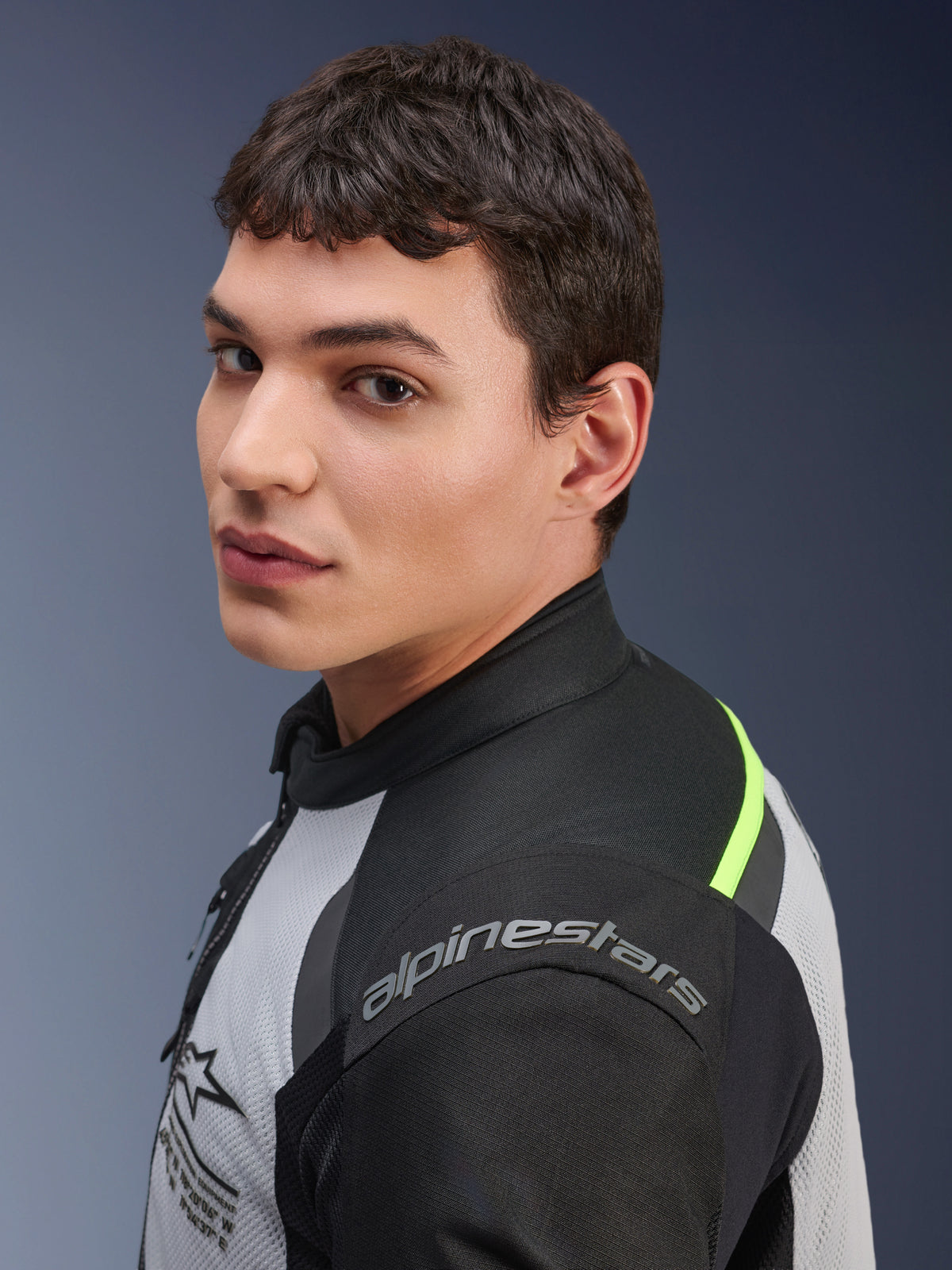 Close-up of a model wearing the Alpinestars Andes Air Drystar® Jacket in Ice Gray, Dark Gray, and Black, featuring neon yellow accents and mesh panels, with Alpinestars branding visible on the shoulder.