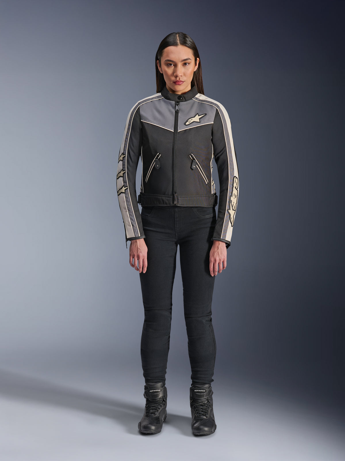 Woman wearing Alpinestars Stella T-Dyno WR Jacket, Black Dark Gray and Ecru, front view, textile motorcycle jacket with vintage-inspired design, featuring chest and sleeve branding, worn with black pants and boots