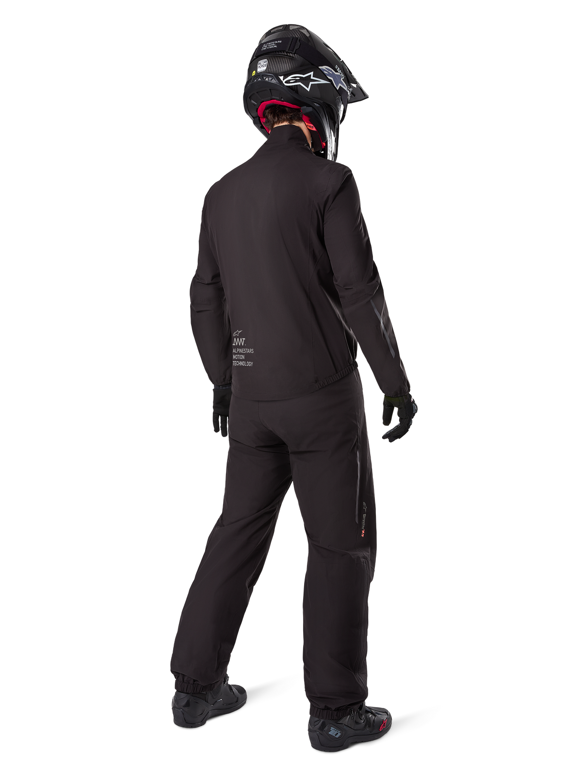 Rider from behind wearing Alpinestars Amt 8 Stretch Drystar® XF liner and pants, all-black technical adventure gear, waterproof and windproof stretch material, matching jacket with 'AMT' branding, black helmet, and boots for a complete all-weather motorcycle touring outfit