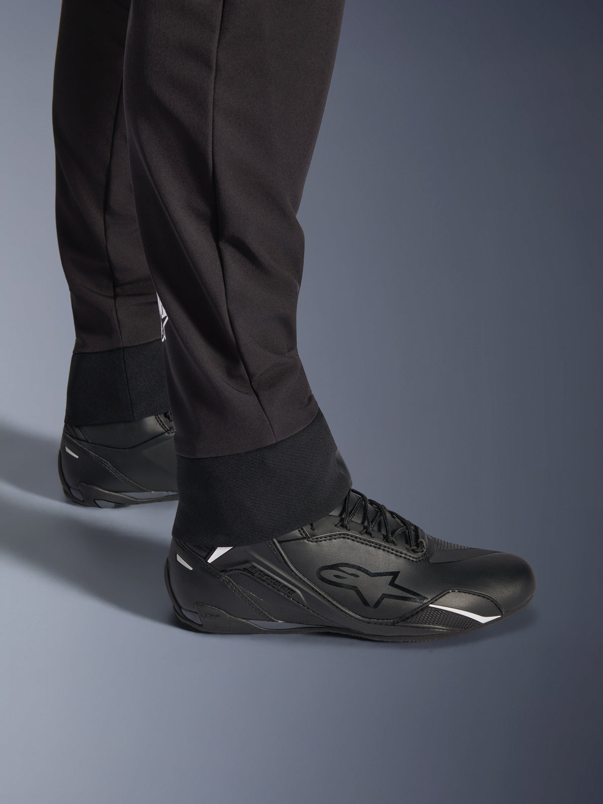Alpinestars Aeroshell Pants, Black, close-up view of the elasticated lower hem and cuff, modern sports softshell design, worn with black Alpinestars riding shoes.