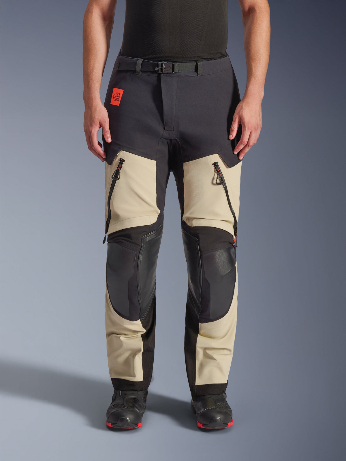 Alpinestars Halo Pro Drystar® XF Laminated Pants, Adventure Motorcycle Pants, Mastic Black, front view worn by a rider, featuring large zippered thigh vents, reinforced black knee panels, and tan textile construction, paired with black and red riding boots