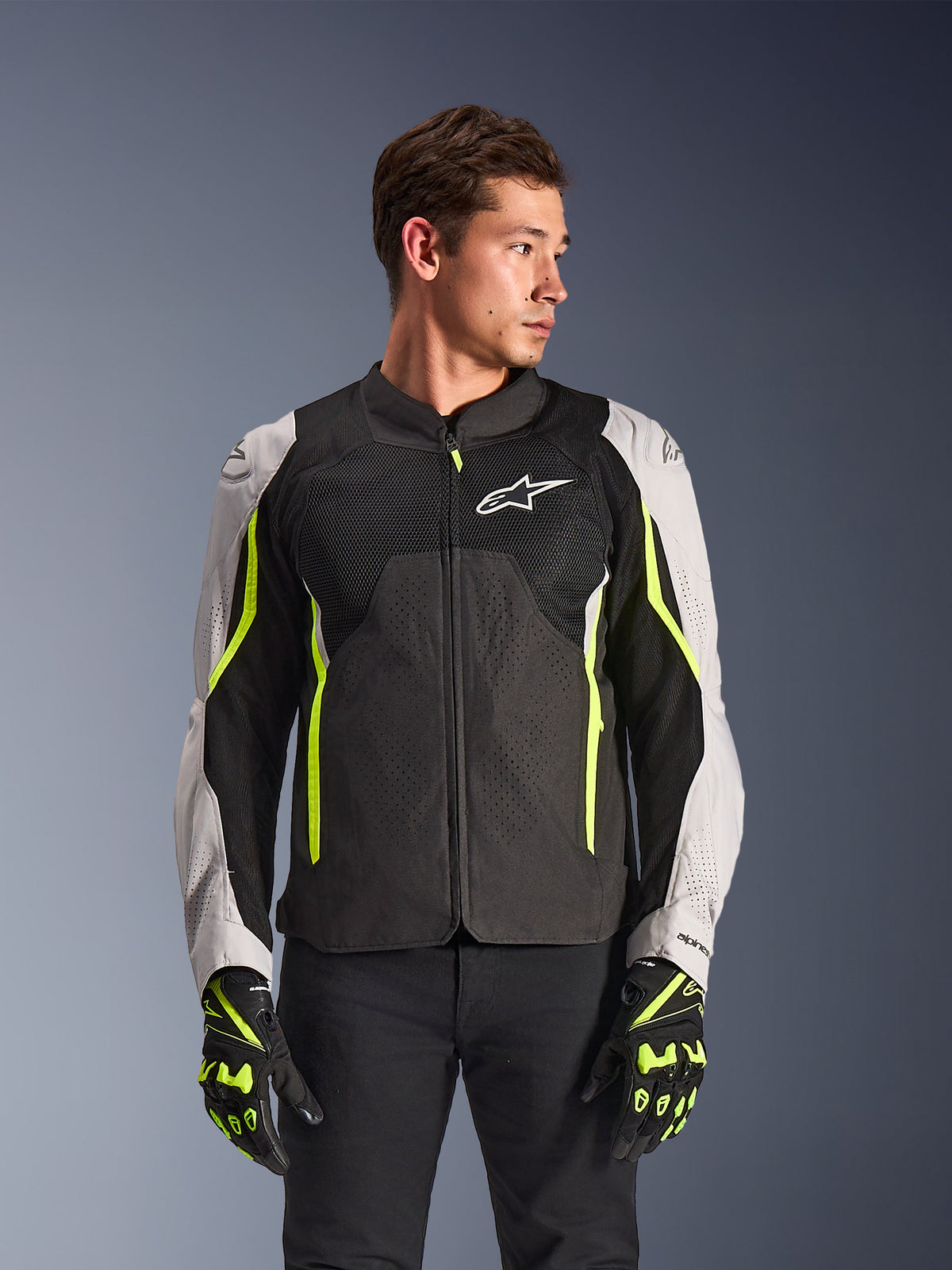 Alpinestars AST V3 Air Jacket, Textile Motorcycle Jacket, Black and Silver with Yellow Fluo accents, featuring large mesh ventilation panels and laser perforations, worn by a model with matching gloves, sport performance riding gear.