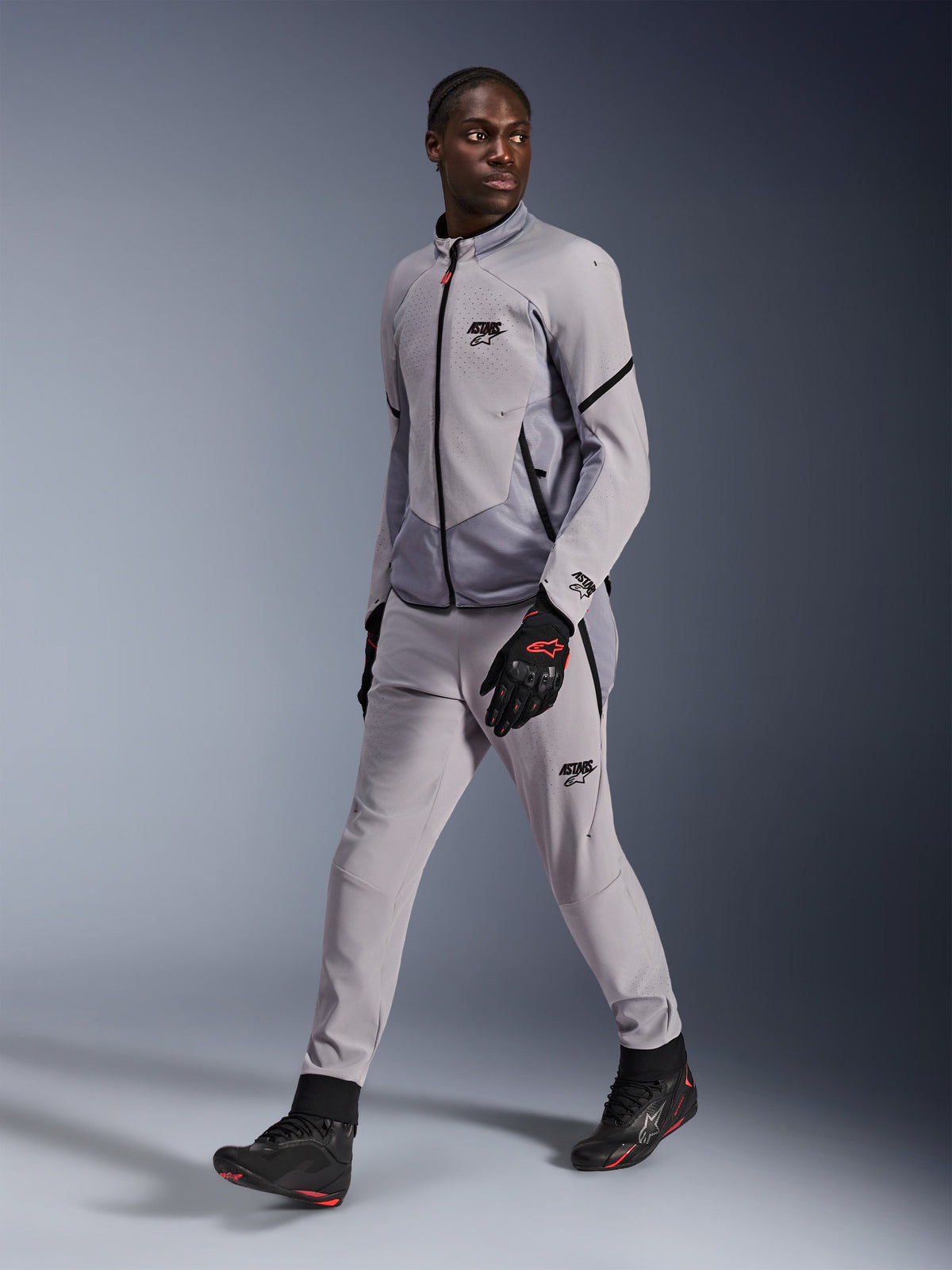 Alpinestars Aeroshell Airflow Jacket in Mid Gray Anthracite, worn by a male model with matching gray riding pants and black gloves, featuring laser-perforated chest ventilation and a sleek sport-cut design.