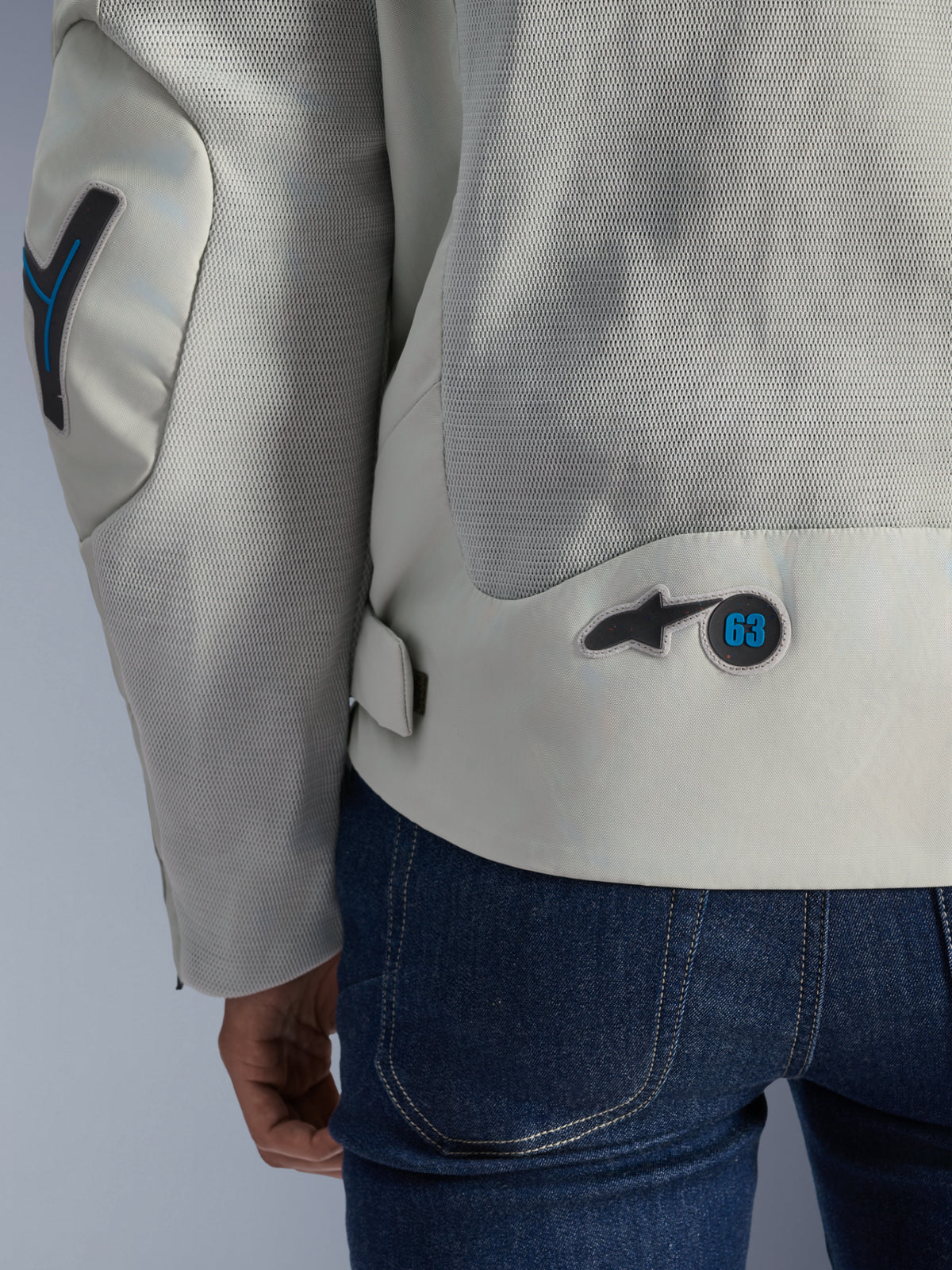 Alpinestars Circal-1 Air Jacket in Metal Gray with Methyl Blue accents, detailed back view highlighting recycled mesh airflow panels and a circular '63' logo badge, worn with blue jeans.