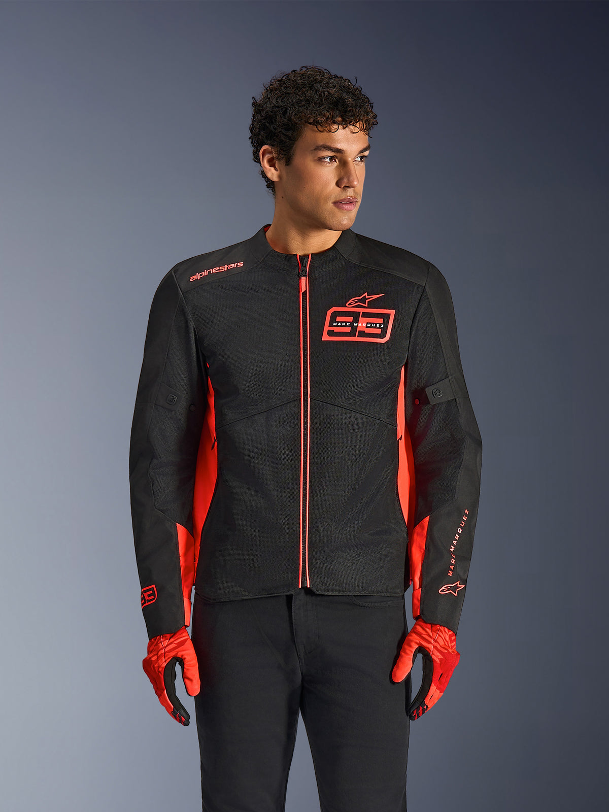 Alpinestars MM93 C-1 Air Jacket, urban motorcycle jacket, Red Fluo and Black, worn by a model with matching red gloves and black pants, featuring bold 93 Marc Marquez chest logo and mesh panels for airflow