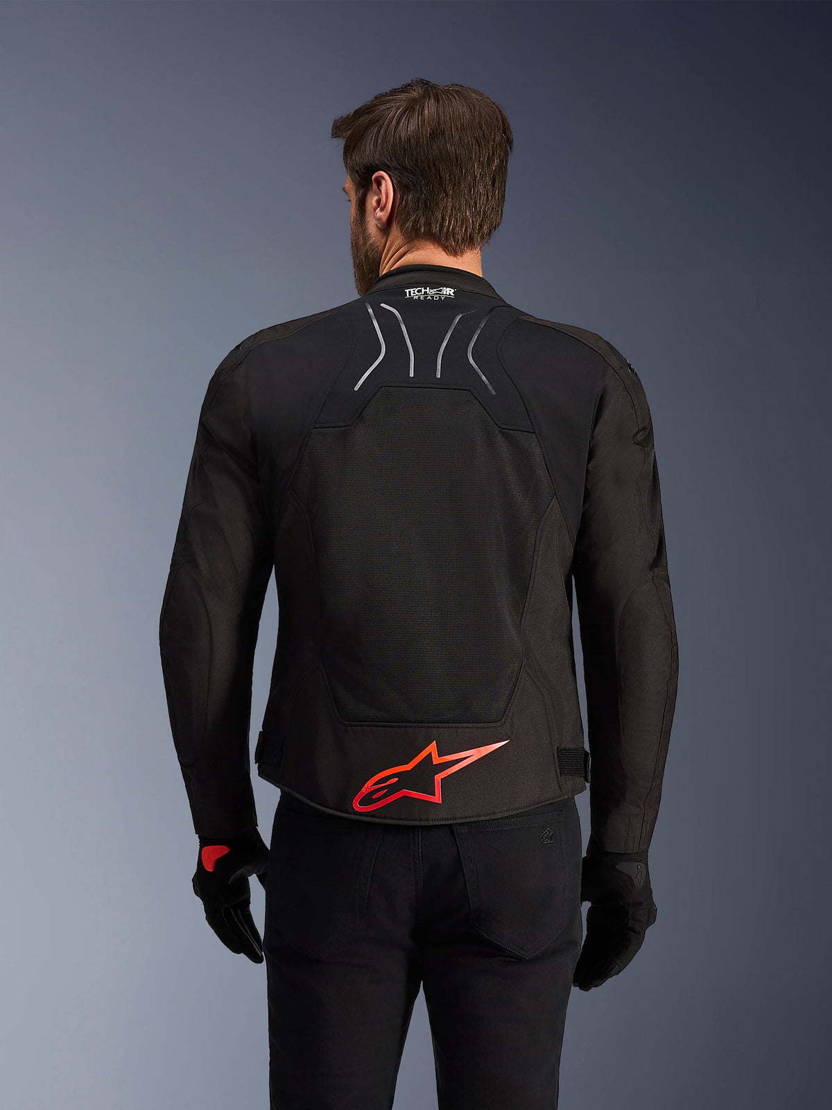 Alpinestars SMX Air Jacket, Rear View, Black with Bright Red Alpinestars logo on the lower back, featuring a high-airflow tech mesh panel and Tech-Air Ready branding, worn by a male rider with black pants and gloves