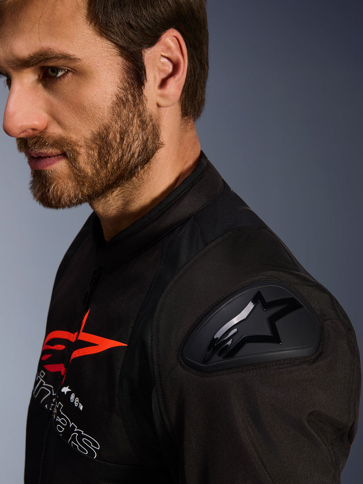 Alpinestars SMX Air Jacket, Black and Red, close-up detail of the DFS Lite shoulder protector with star logo, worn by a man with a beard, textile racing and sport motorcycle jacket.