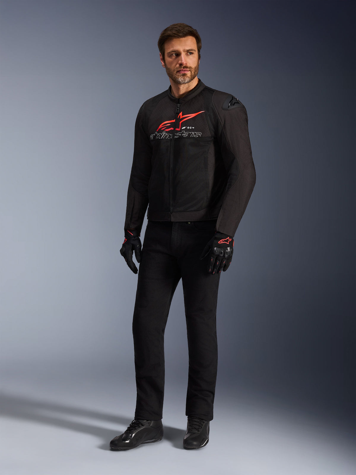 Male model wearing the Alpinestars SMX Air Jacket in Black Bright Red White, styled with black technical pants, black and red gloves, and black riding shoes, featuring a prominent red chest logo and white branding, full-body studio shot for sport motorcycling gear
