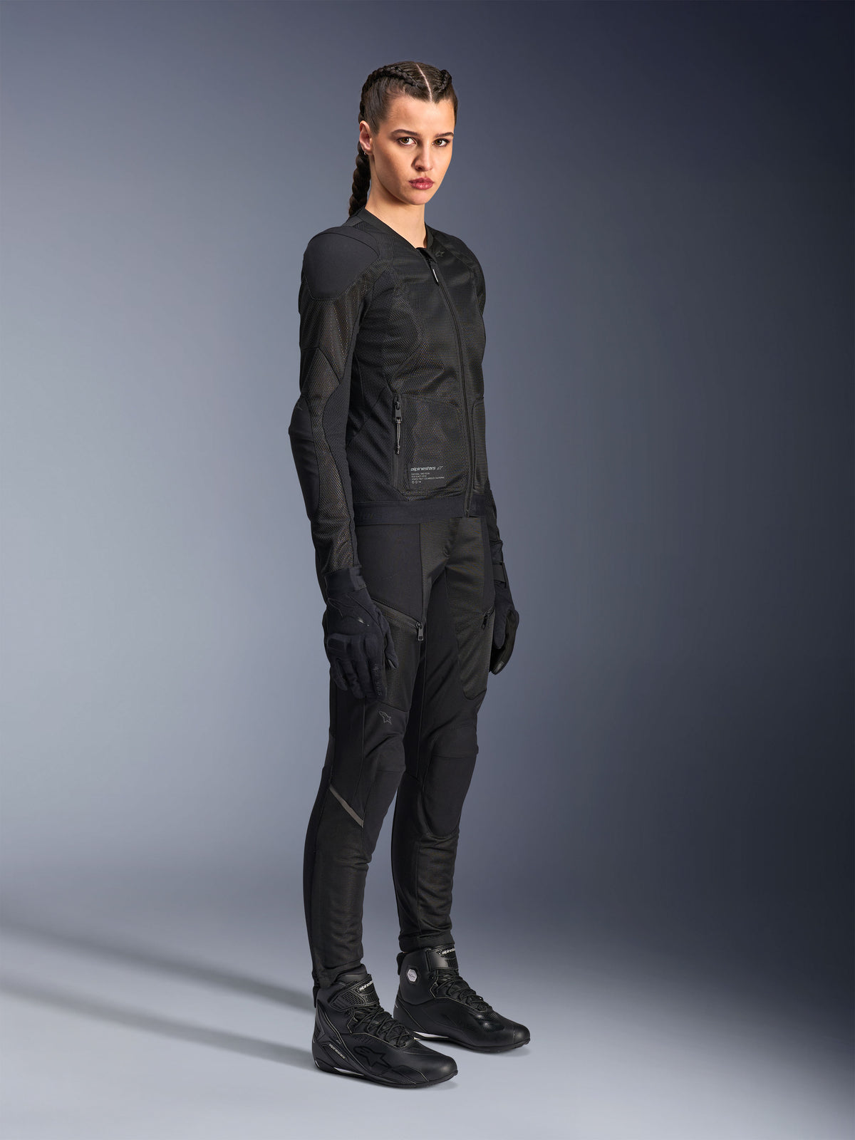 Female rider wearing the Alpinestars Stella Troop-Air Jacket in Black, featuring technical 2D mesh construction, paired with matching black motorcycle pants, gloves, and boots, styled for urban riding.